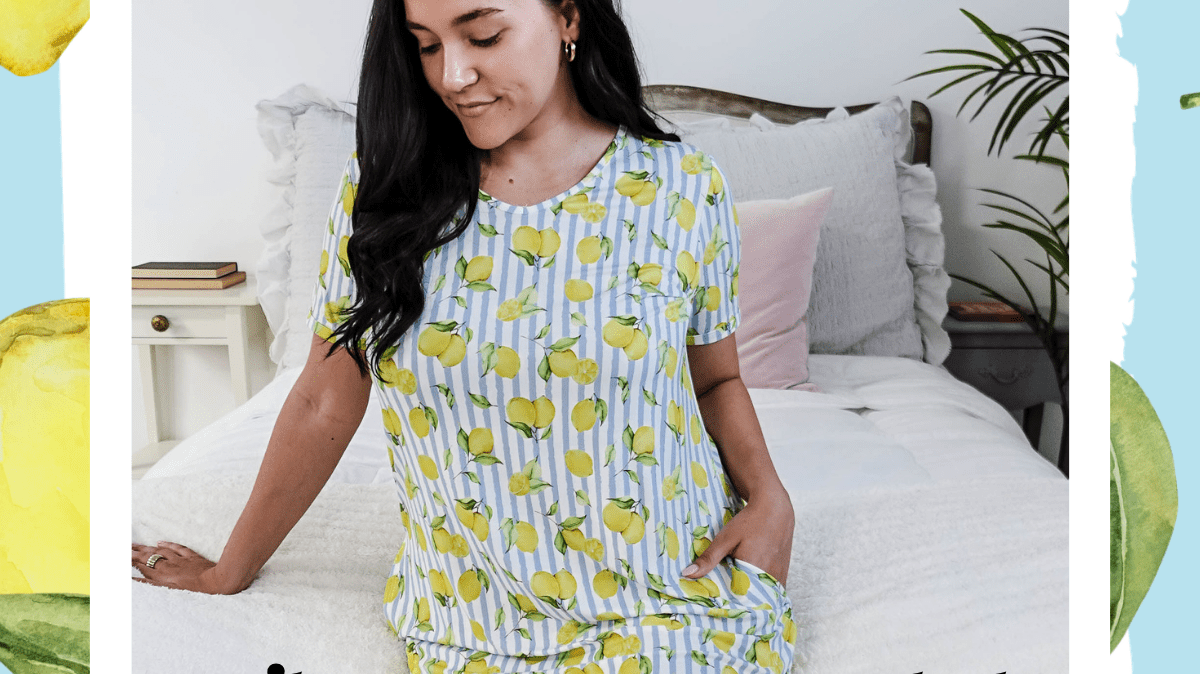 Woman wearing lemon-print bamboo pajama set from the Cloud Nine Pajamas Summer Citrus Dreamers Club box, sitting on a bed.