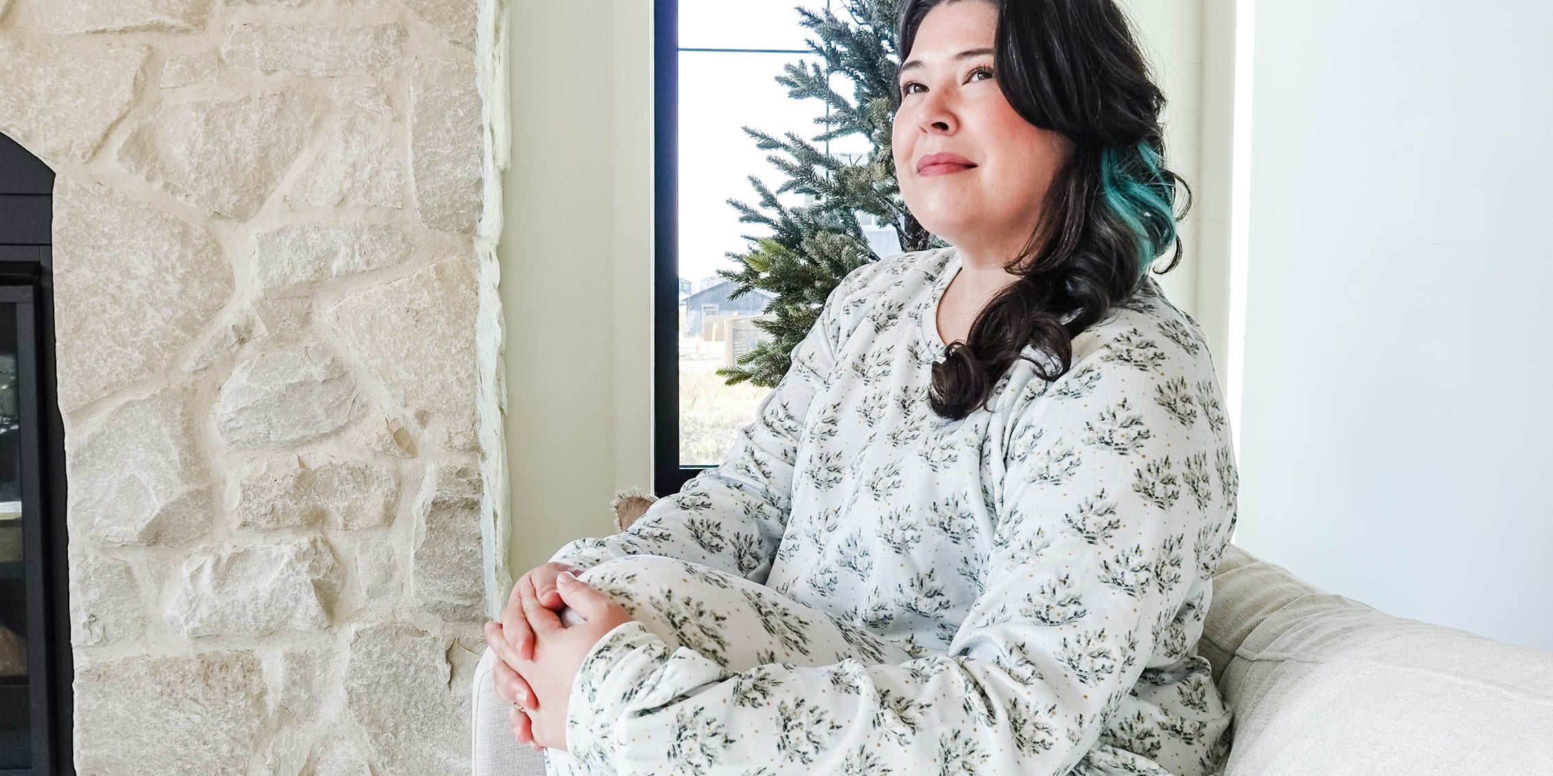 Woman sitting in cozy Miranda Nic Loungewear in a stylish living room with a fireplace and a Christmas tree.