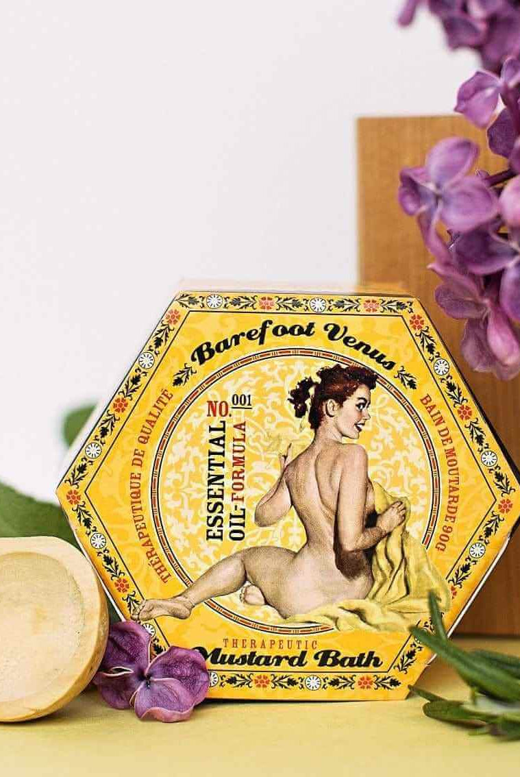 Mustard Bath Detox Bath Salts packaging featuring woman illustration, surrounded by purple flowers and a wooden spoon.