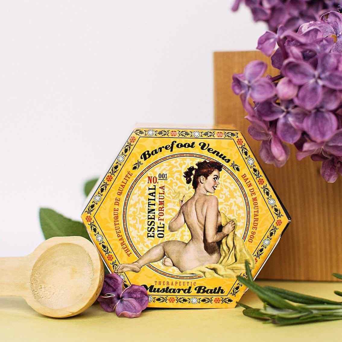 Mustard Bath Detox Bath Salts packaging featuring woman illustration, surrounded by purple flowers and a wooden spoon.