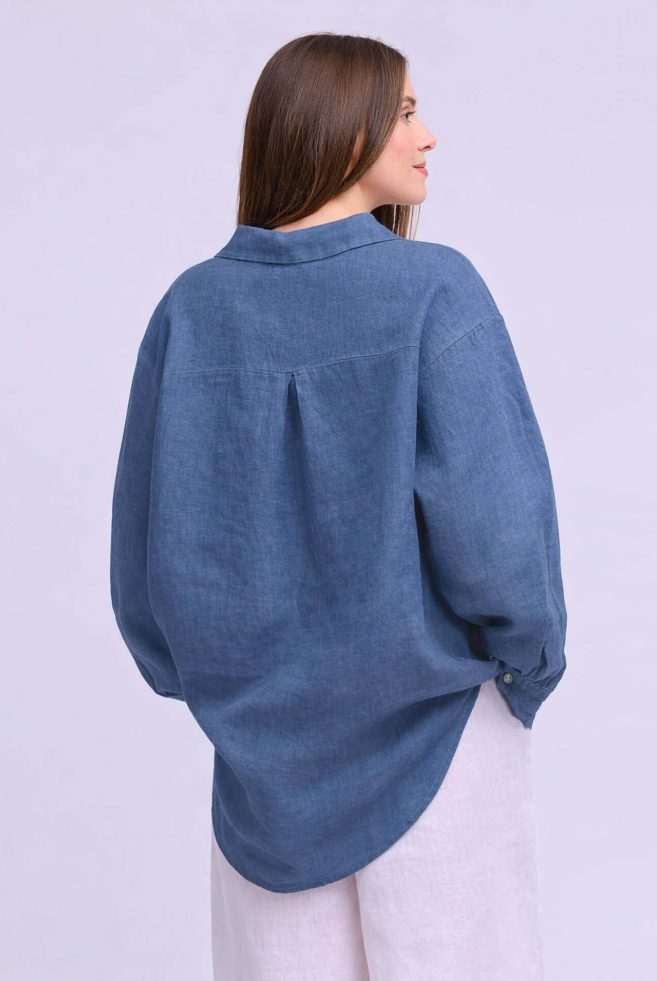 Back view of a model wearing the Yoga Jeans Elena Linen Oversized Button Up Top in denim blue.