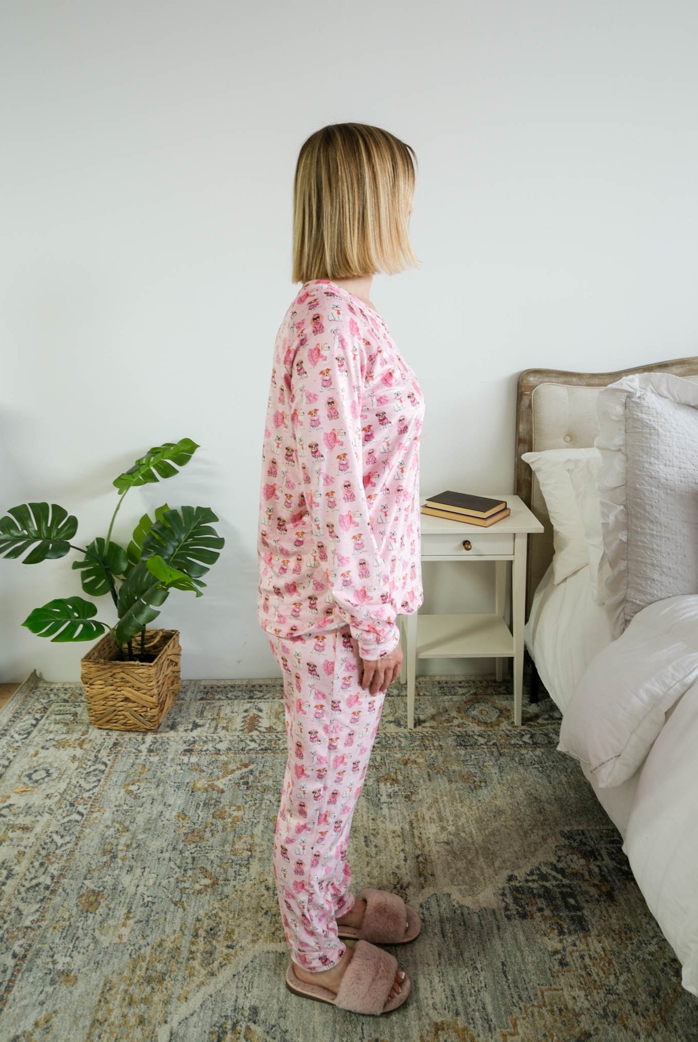Side profile on model in bedroom of Miranda Nic women's pink velour long sleeve top and jogger pants loungewear set featuring Chic Puppies dog print - Cloud Nine Pajamas