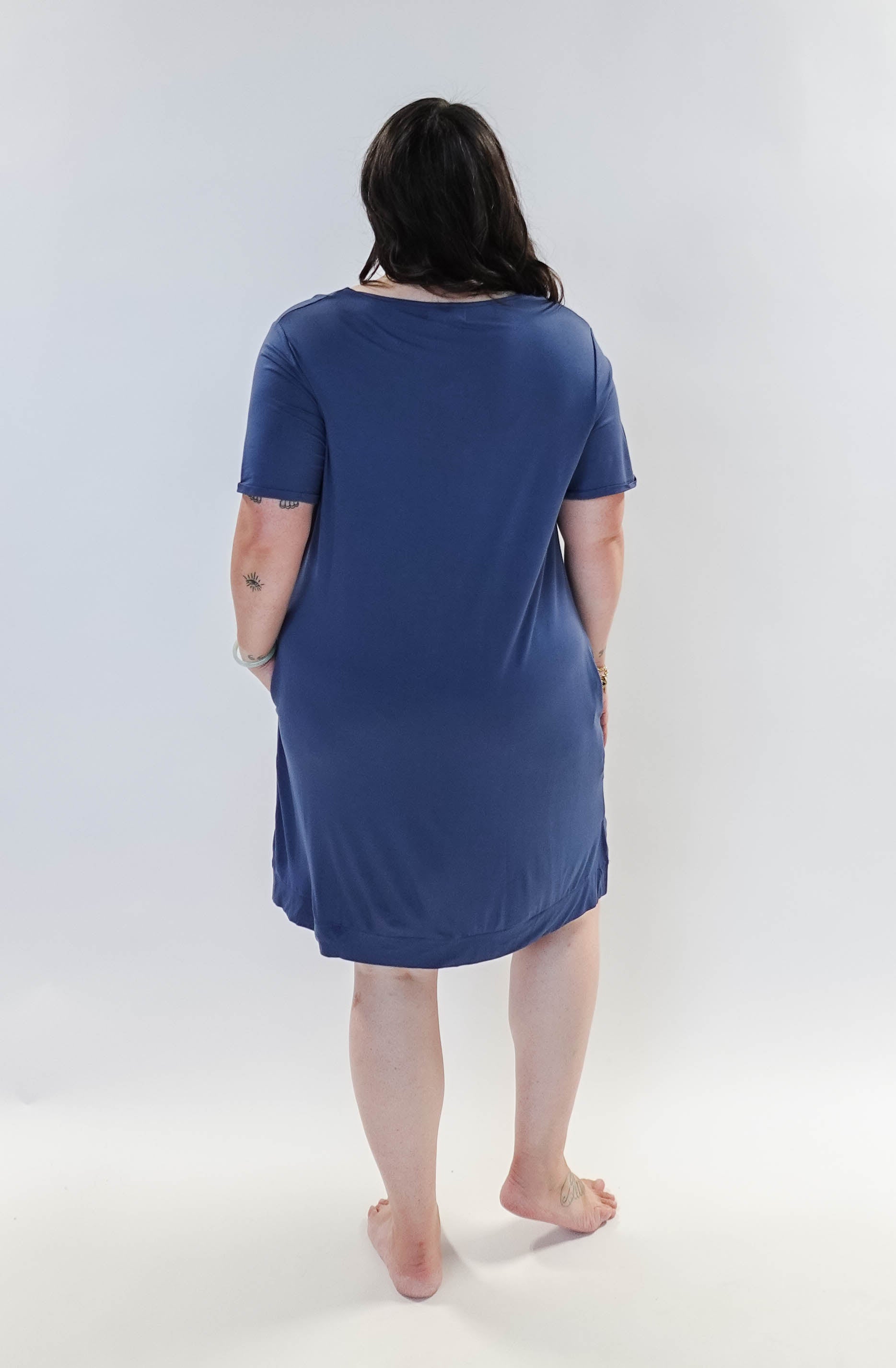 Stylish model wearing Denim Blue V Neck Bamboo Nightshirt dress with pockets, showcasing versatility in sleepwear and everyday fashion. Showing back view