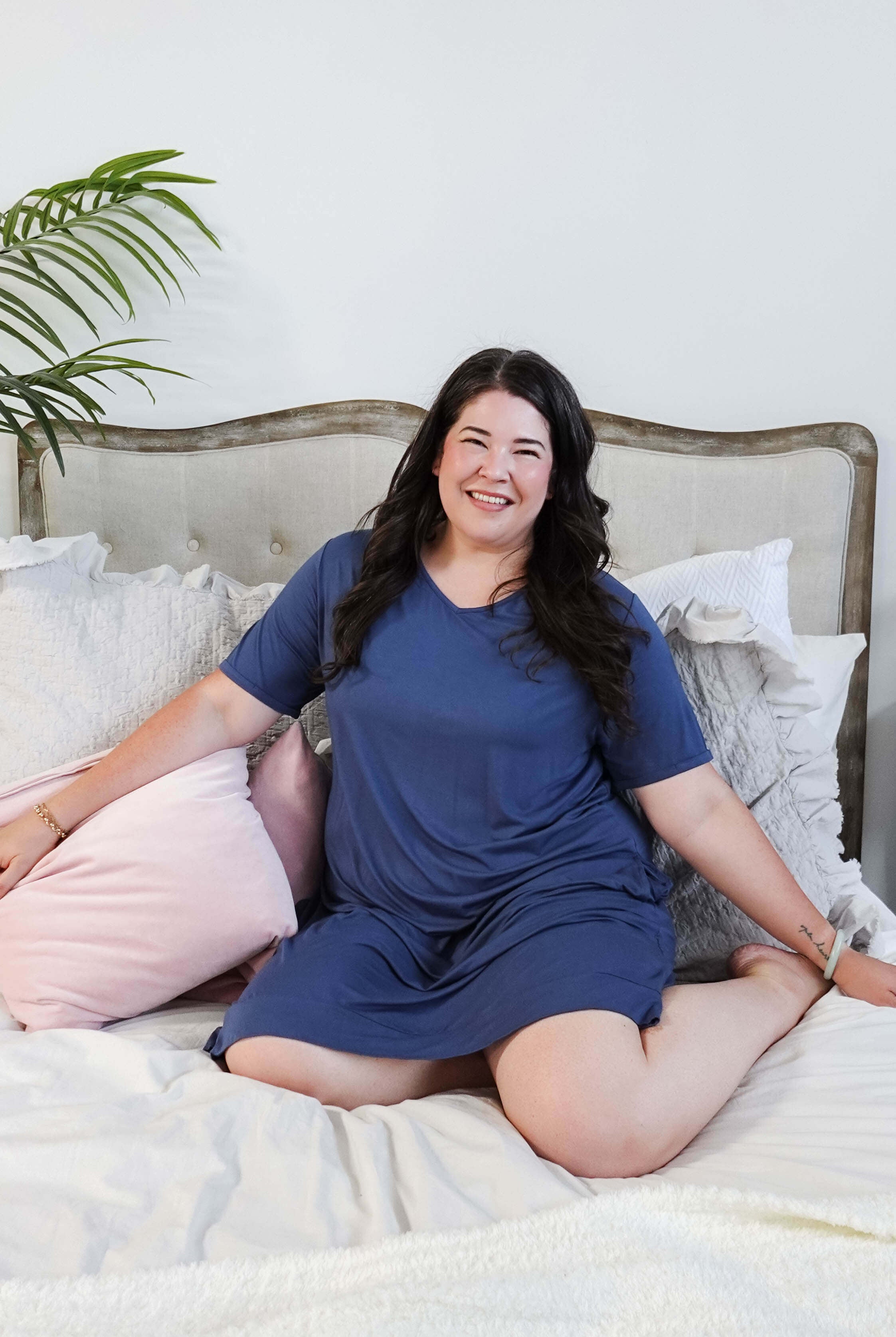 Stylish model wearing Denim Blue V Neck Bamboo Nightshirt dress with pockets, showcasing versatility in sleepwear and everyday fashion. Justine Mah lounges in bed wearing the dress.