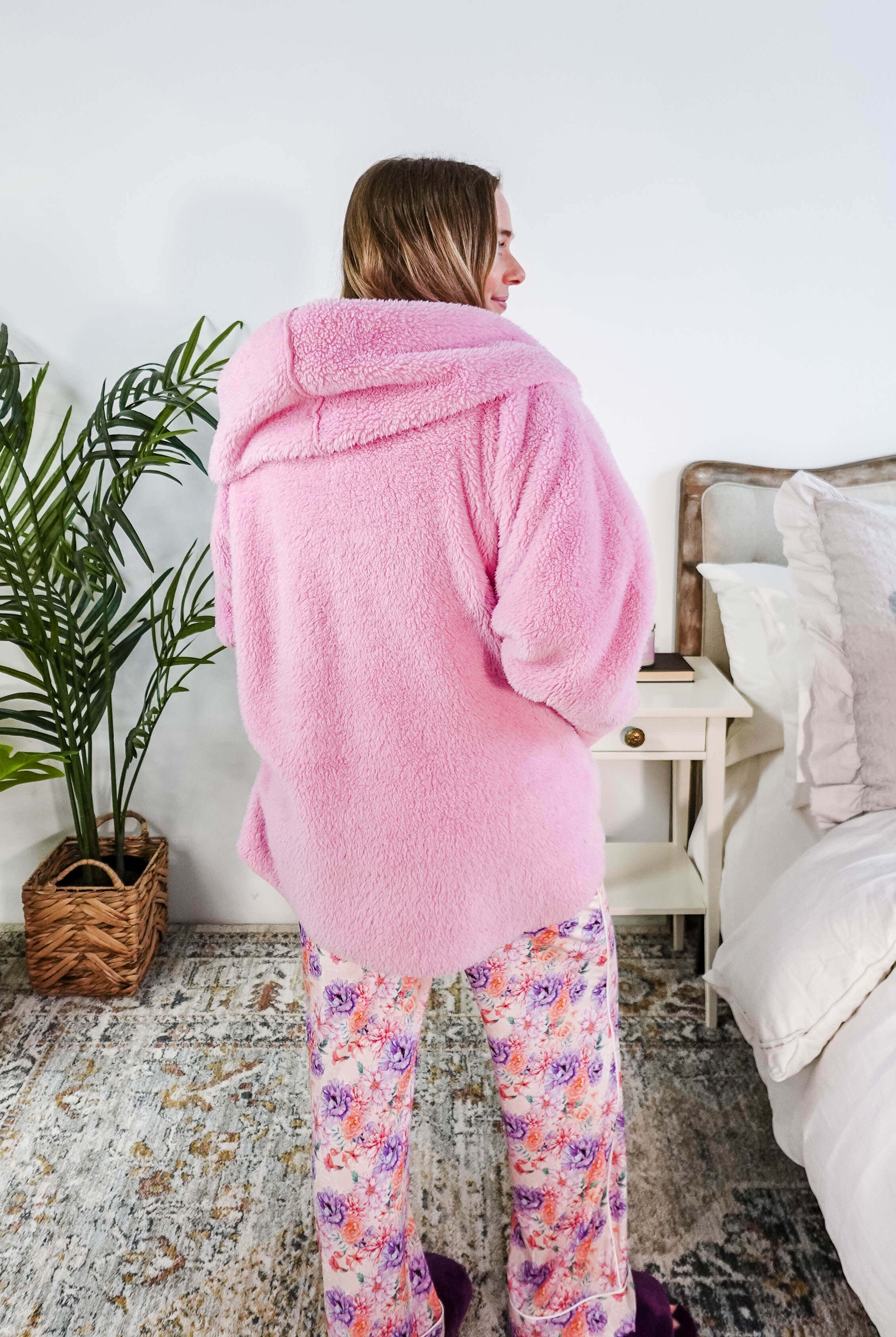 Woman wearing an Essential Hooded Fluffy Cozy Cardigan with Pockets in pink, standing in a cozy bedroom.
