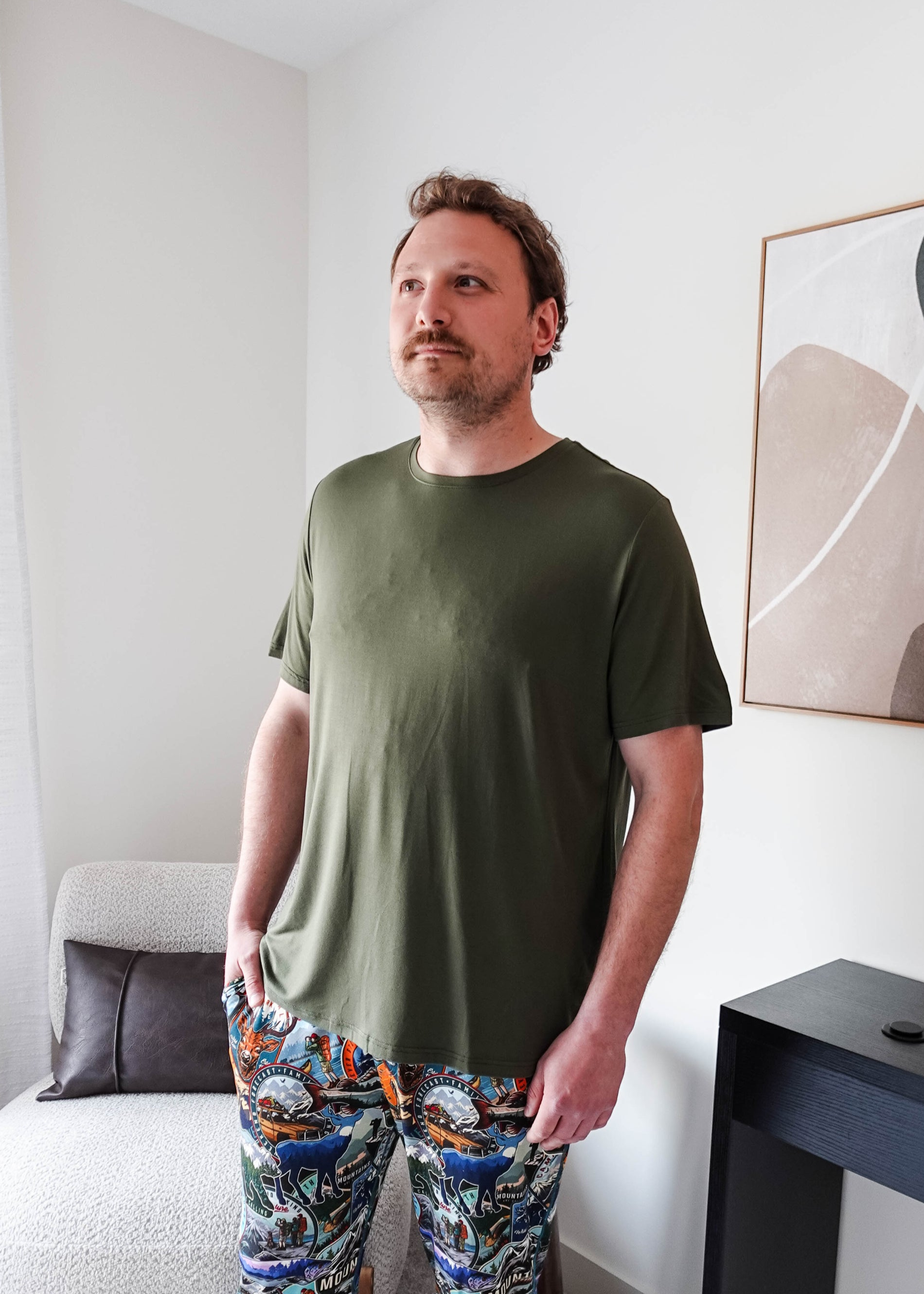 Man wearing the Olive Forest Unisex Short Sleeve Tee Bamboo with colorful patterned pants in a modern interior.