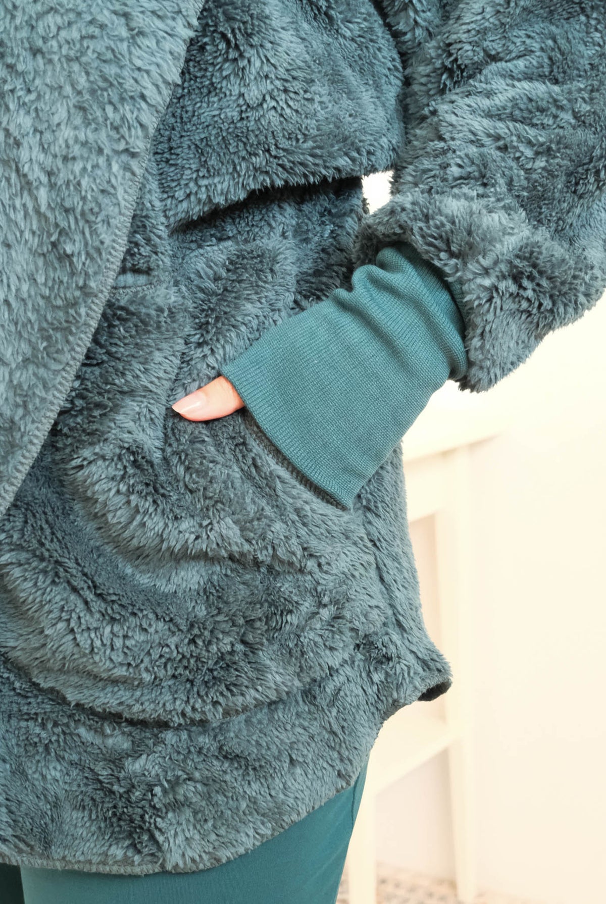 Close-up of a person wearing a plush, textured dark teal fleece cardiganwith a matching ribbed knit cuff and dark midnight teal bamboo pajama pants, with a hand in a pocket. Cloud Nine Pajamas Edmonton