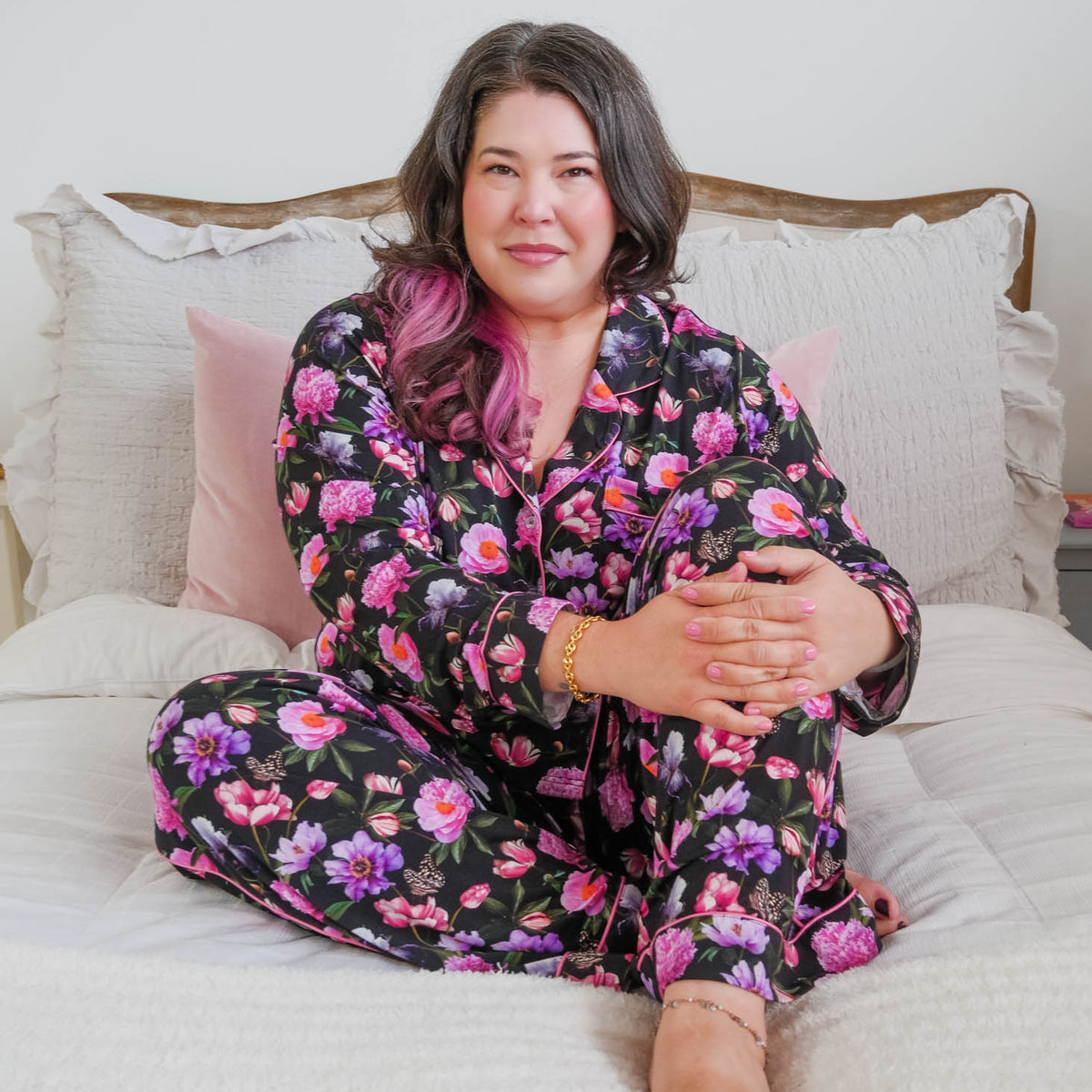 Lifestyle photo on plus size model in bedroom setting Georgia Rylan women's bamboo long sleeve button-up top and straight-leg pajama pants in Dreamy Blooms black floral print - Cloud Nine Pajamas