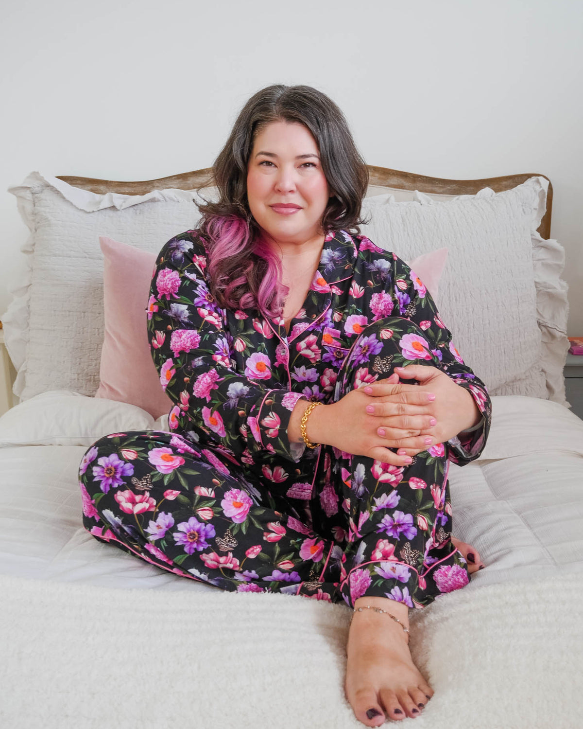 Lifestyle photo on plus size model in bedroom setting Georgia Rylan women's bamboo long sleeve button-up top and straight-leg pajama pants in Dreamy Blooms black floral print - Cloud Nine Pajamas