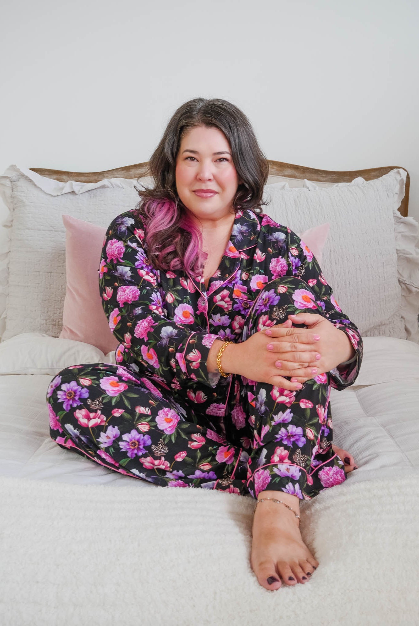 Lifestyle photo on plus size model in bedroom setting Georgia Rylan women's bamboo long sleeve button-up top and straight-leg pajama pants in Dreamy Blooms black floral print - Cloud Nine Pajamas
