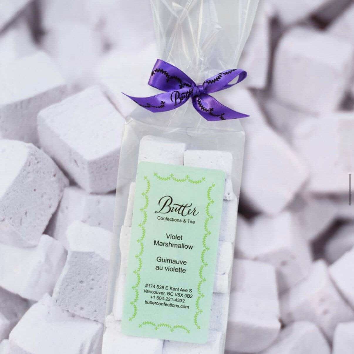 Handcrafted Gourmet Marshmallows in a clear bag with a purple ribbon on a background of fluffy marshmallows.