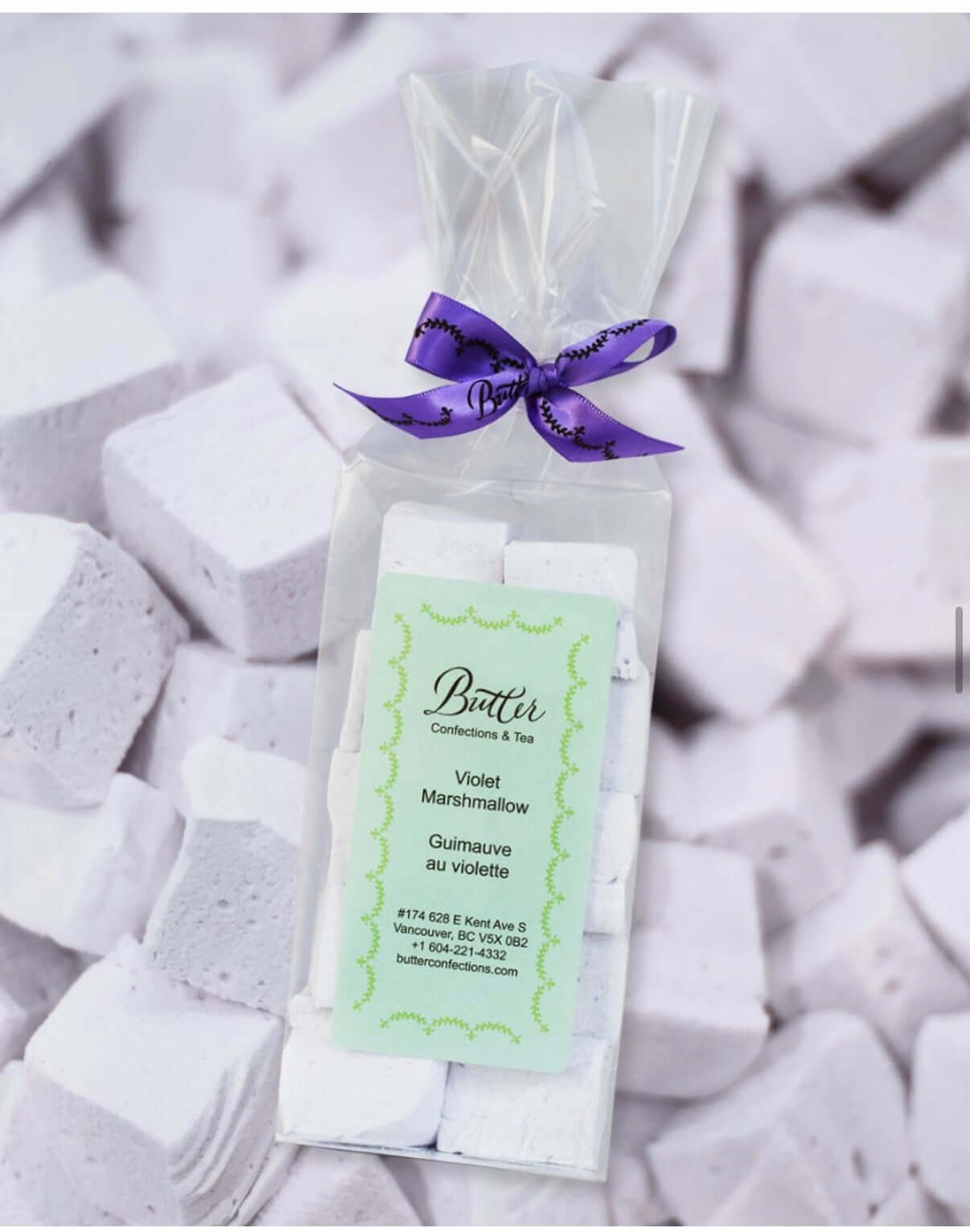 Handcrafted Gourmet Marshmallows in a clear bag with a purple ribbon on a background of fluffy marshmallows.