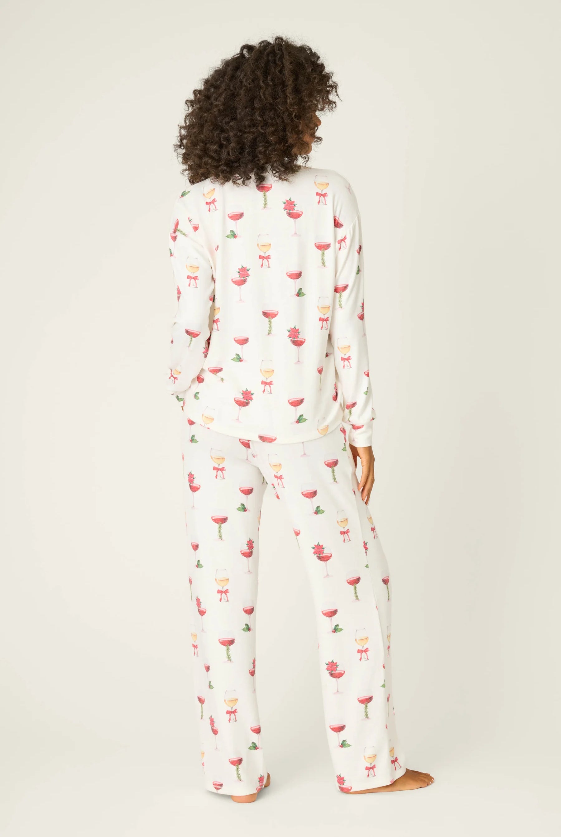Let's Get Toasty Holiday Wine Print PJ Set | Champagne | PJ Salvage Women's set with champagne coupes with red liquid and holly, poinsettia and bows on an ivory background, showing the back of the pj set
