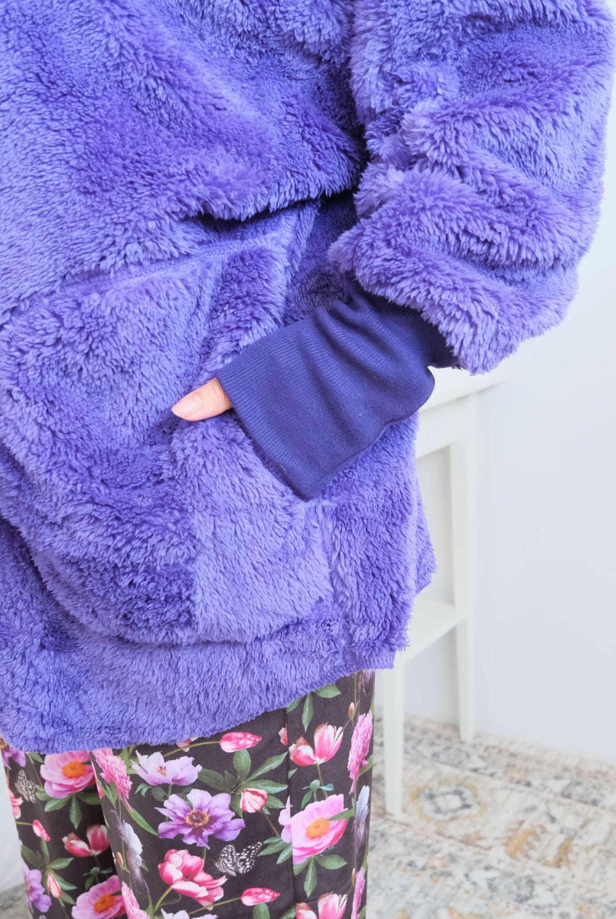 Close-up of a woman wearing the purple fluffy hooded cardigan by Jan Marie open over a black top, showing the plush sherpa-like texture, wide lapel, and pruple ribbed cuff at the wrist with one hand tucked into the front pocket. Cloud Nine Pajamas Edmonton