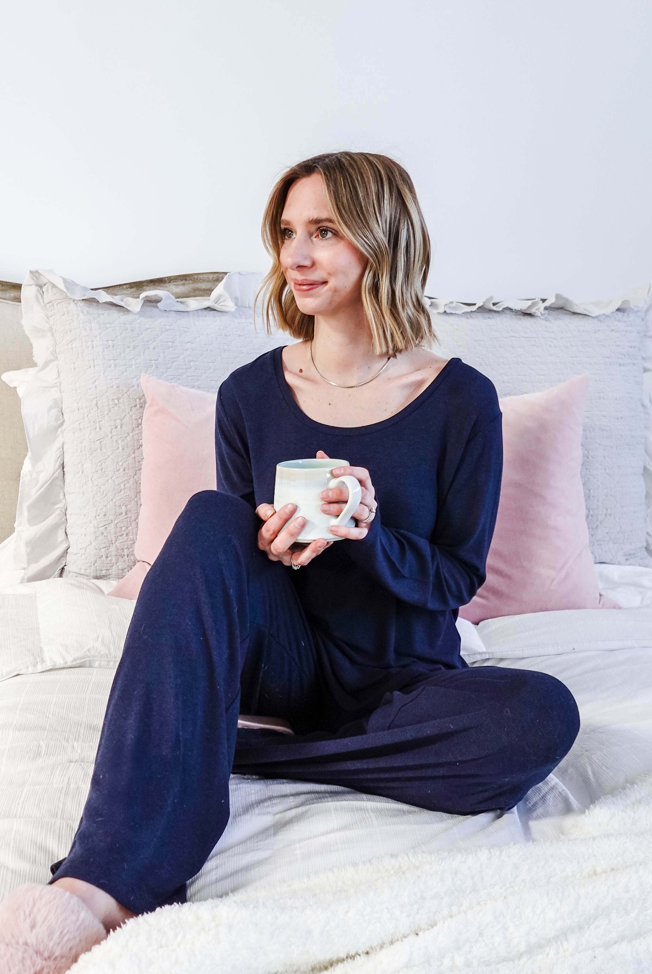 Miranda wearing the Navy Melange Top Straight Pant Knit Lounge Set, highlighting the boat-neck top and flowy trousers - lifestyle shot on bed holding coffee cup