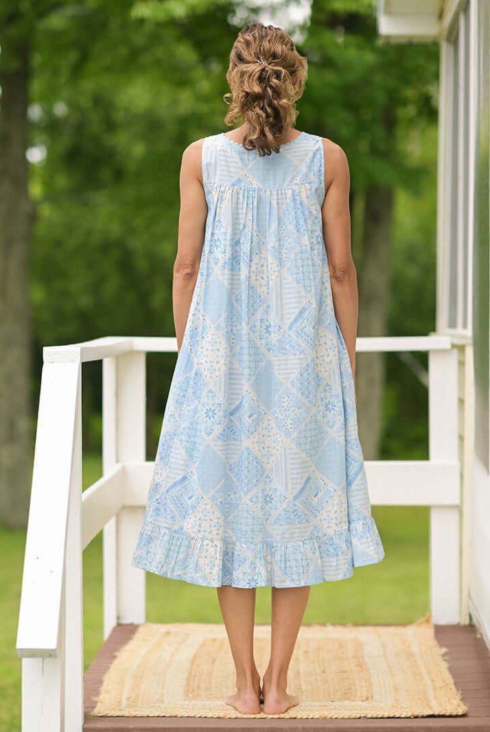 Showing the back of the April Cornell Maddie’s Medley Cotton Nightgown – Embroidered Light Blue Sleeveless Nighty with Button Front. Worn by a model in a cottage/outdoor setting