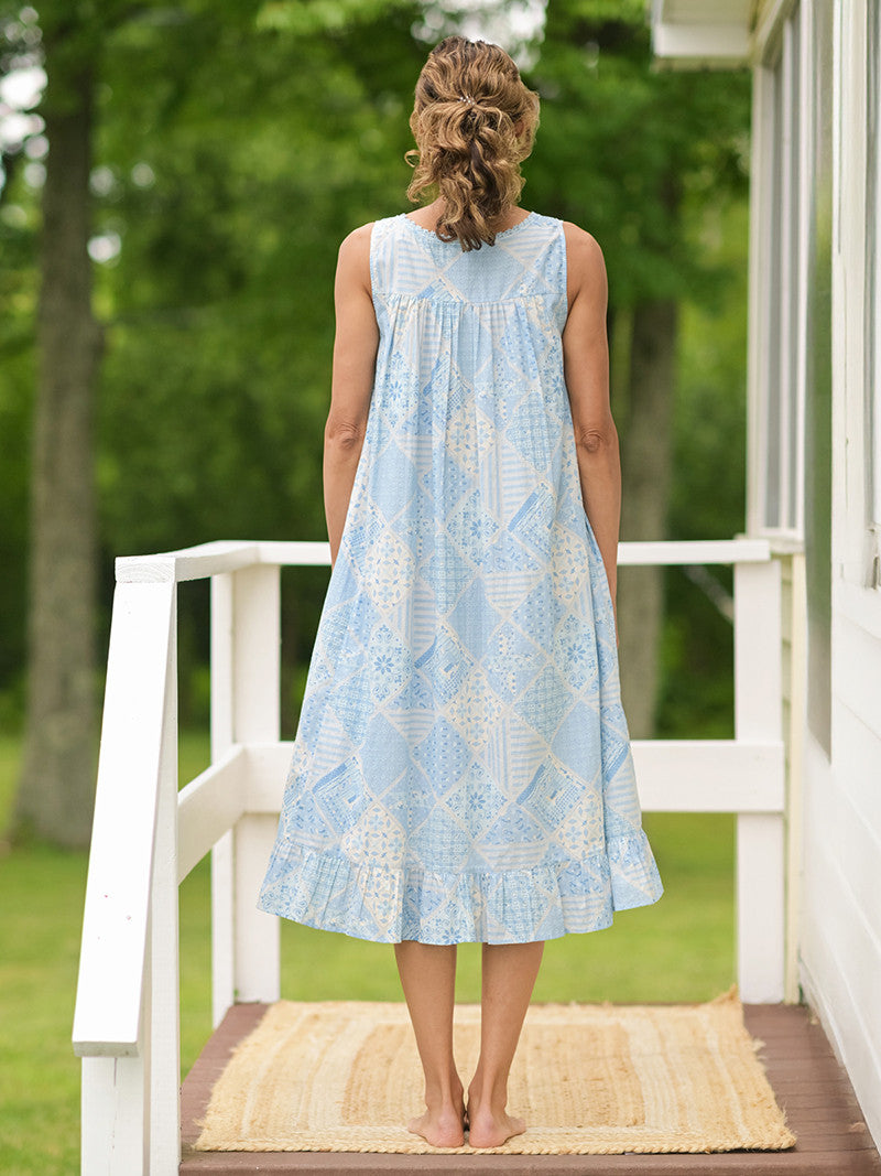 Showing the back of the April Cornell Maddie’s Medley Cotton Nightgown – Embroidered Light Blue Sleeveless Nighty with Button Front. Worn by a model in a cottage/outdoor setting