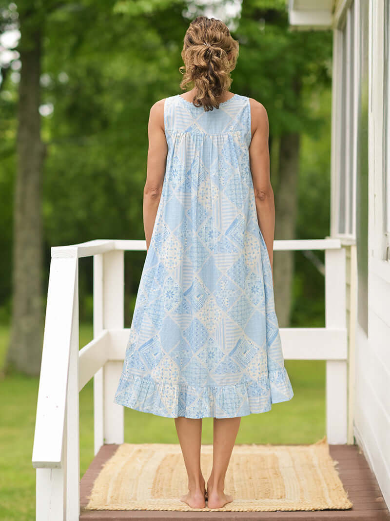 Showing the back of the April Cornell Maddie’s Medley Cotton Nightgown – Embroidered Light Blue Sleeveless Nighty with Button Front. Worn by a model in a cottage/outdoor setting