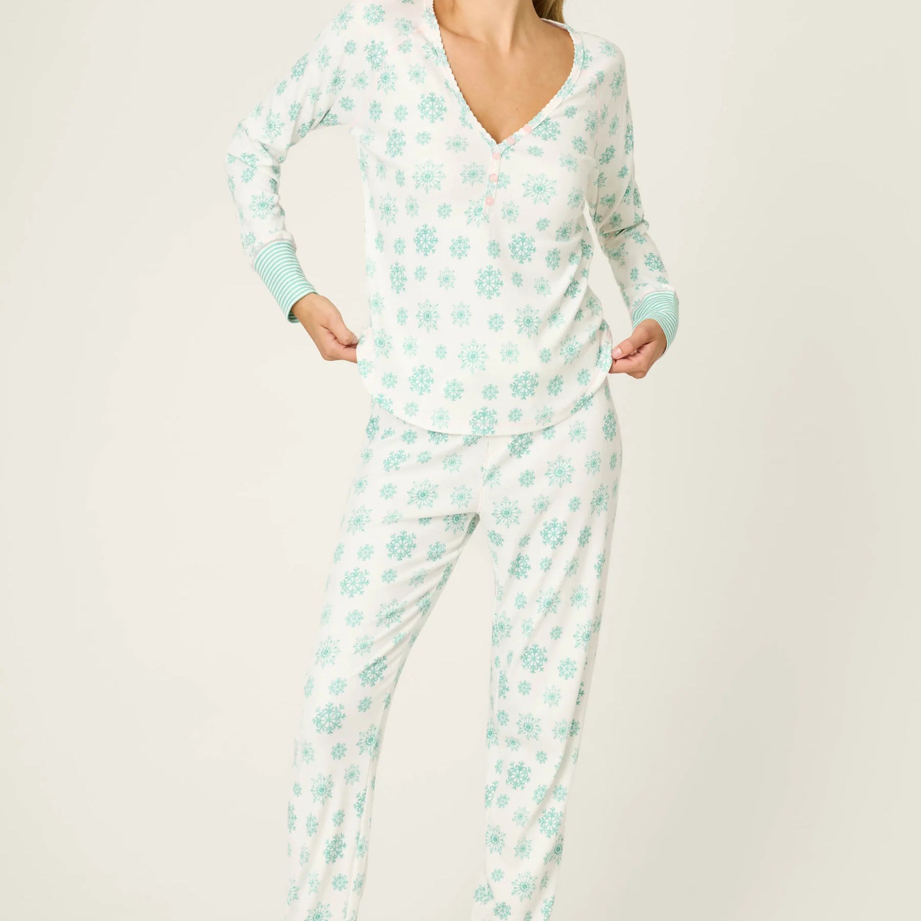 Model (Alexis, 5'8") wearing the PJ Salvage Snowflake Wishes Pointelle PJ Set, showing the ivory V-neck henley top with striped cuffs and jogger pants with a pink tie in the green snowflake print.