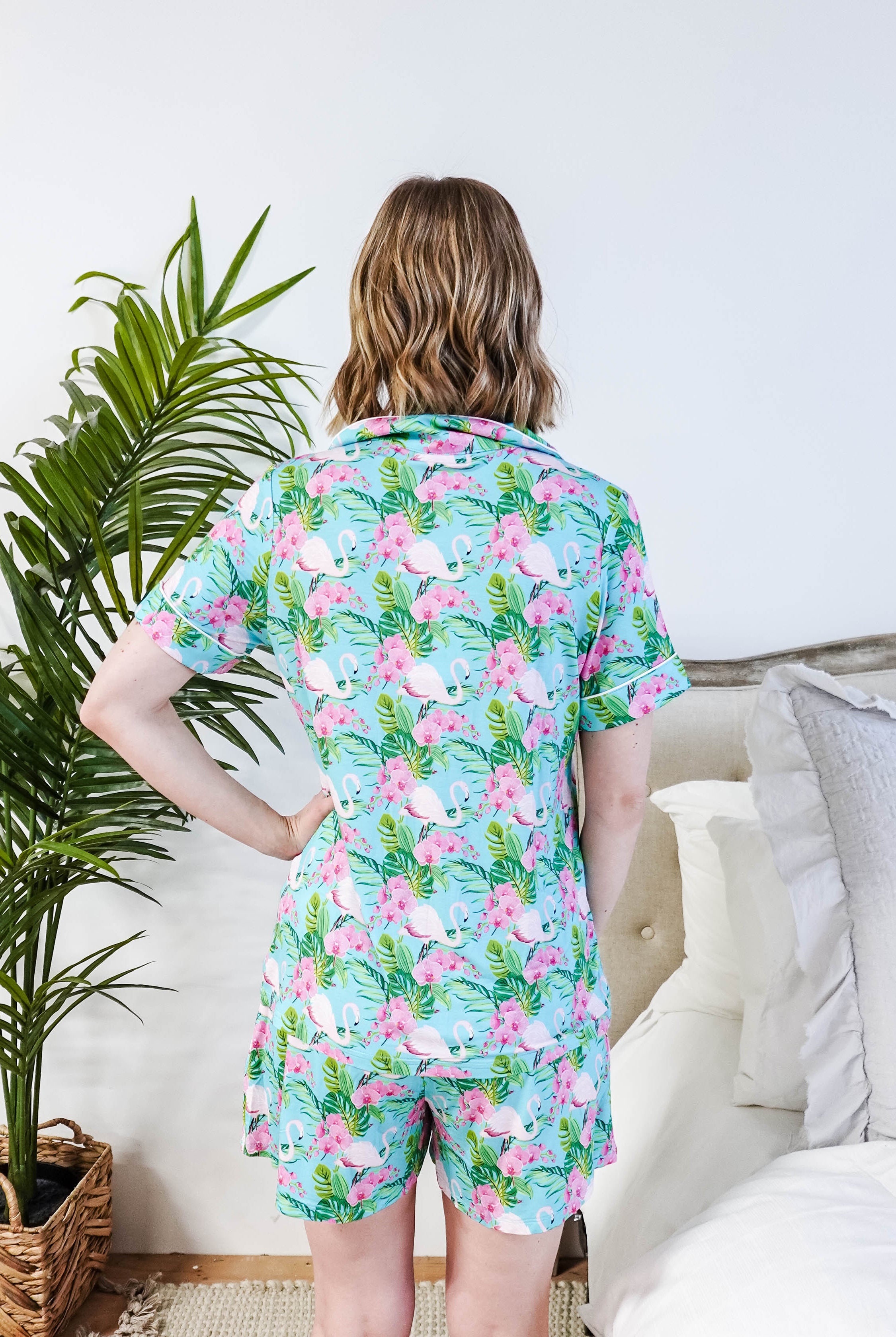 Back view of a woman wearing the Tropic Like It's Hot Bamboo Short Sleeve Pajama Set by Georgia Rylan, featuring a vibrant flamingo print.