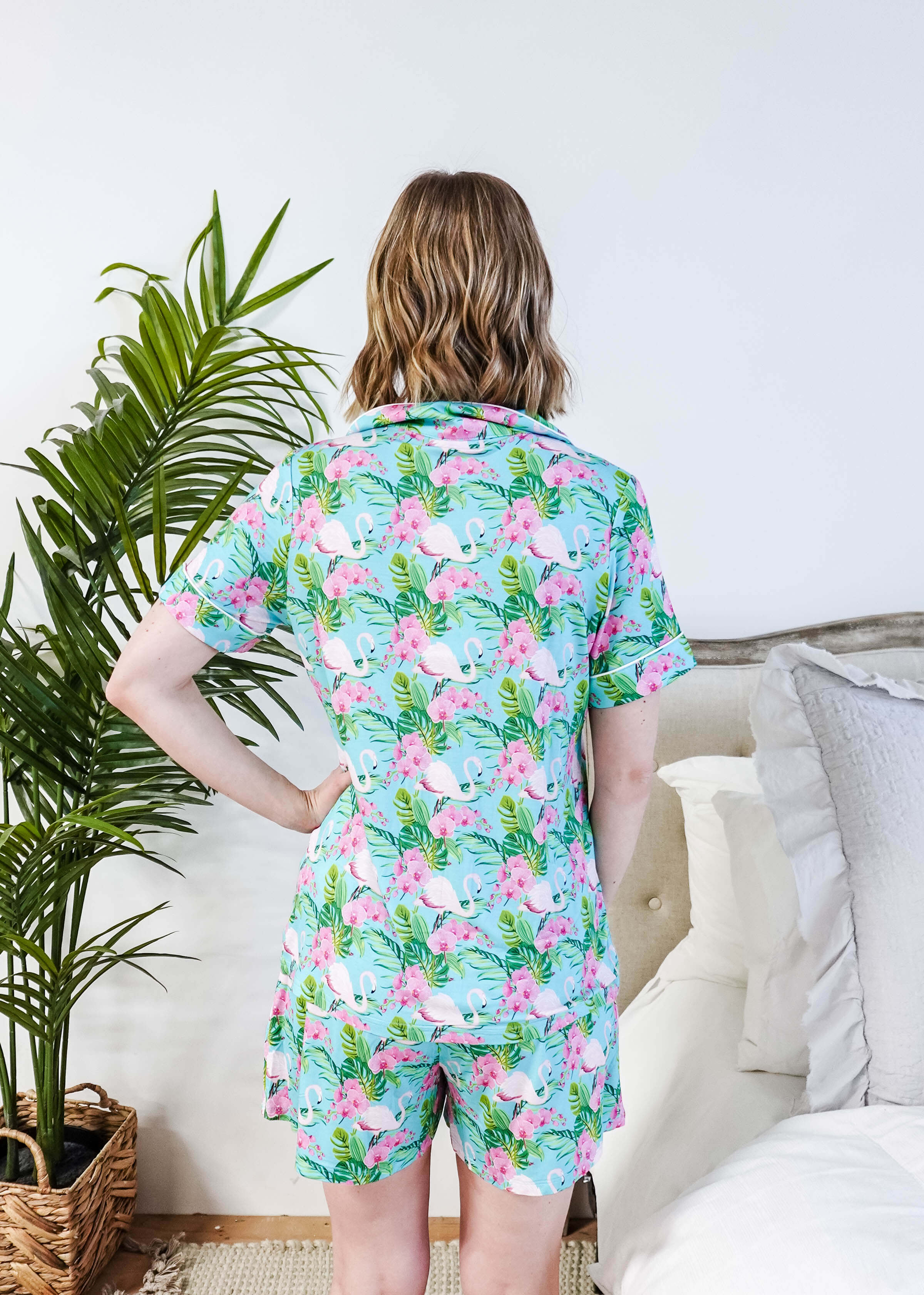 Back view of a woman wearing the Tropic Like It's Hot Bamboo Short Sleeve Pajama Set by Georgia Rylan, featuring a vibrant flamingo print.