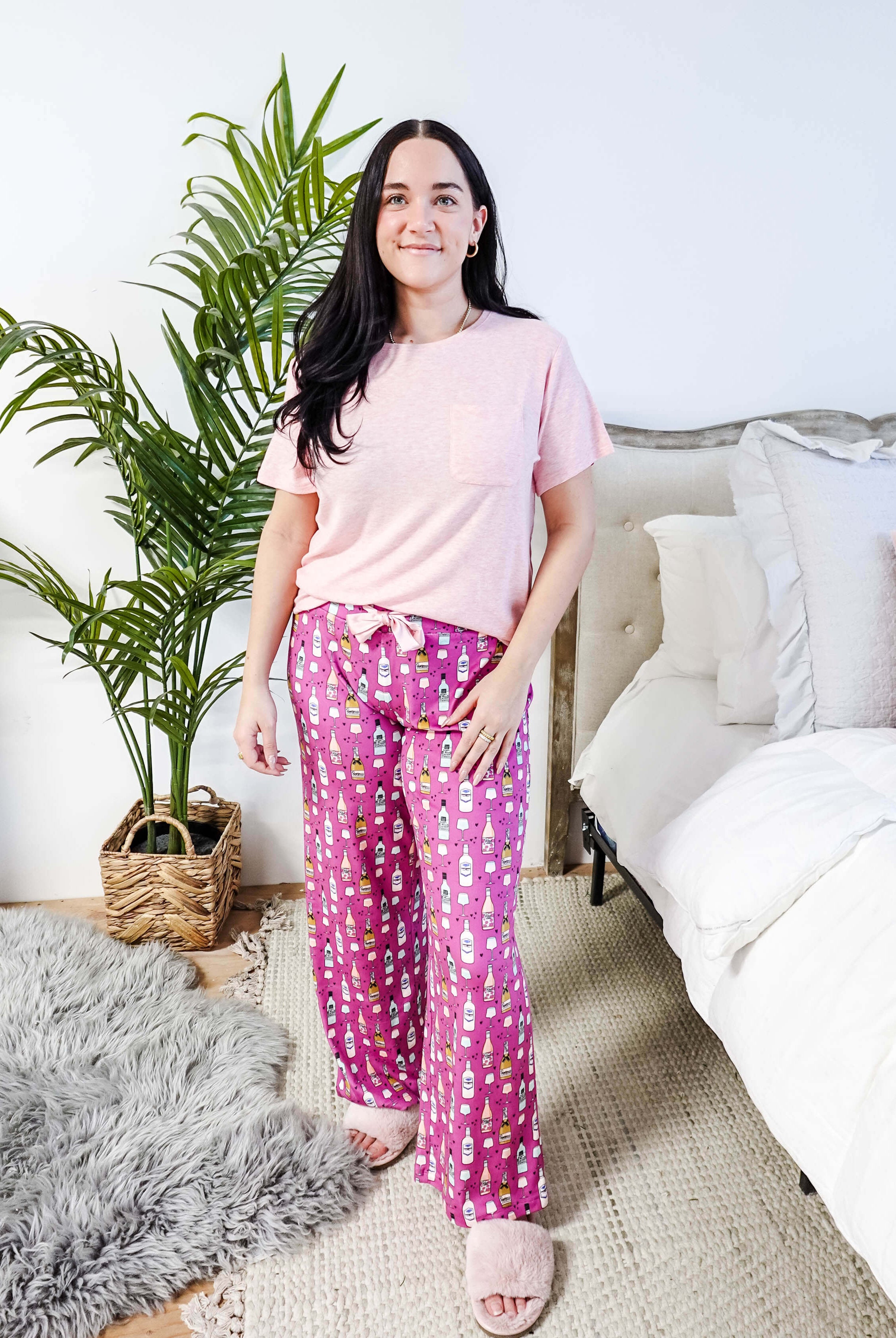 Sydney wearing the Wine Down velvety velour pajama set featuring hot pink wine print pants and a light pink pocket tee.