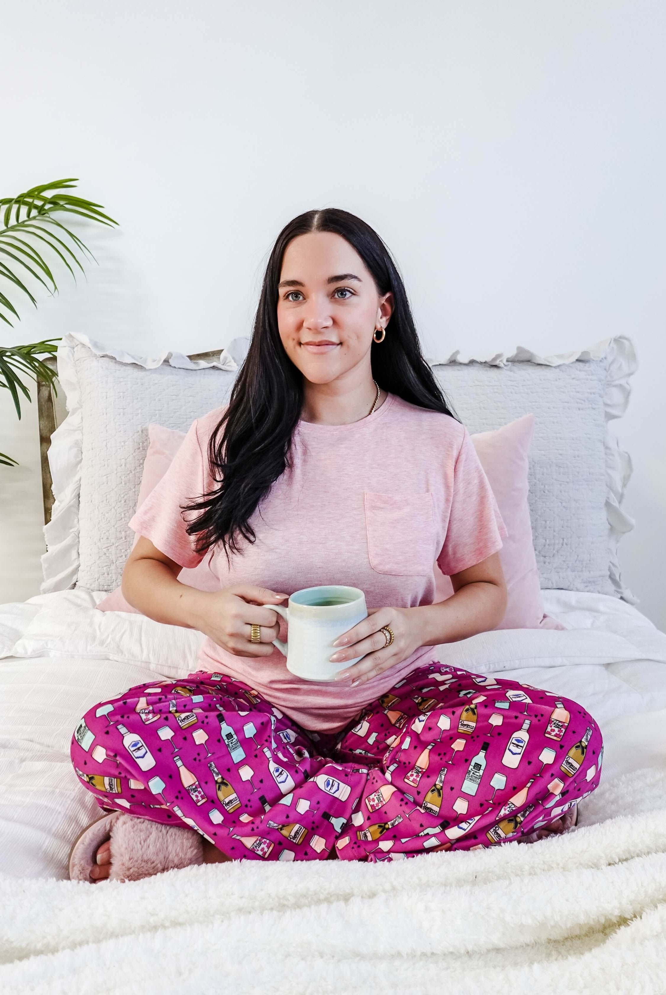 Sydney wearing the Wine Down velvety velour pajama set featuring hot pink wine print pants and a light pink pocket tee.