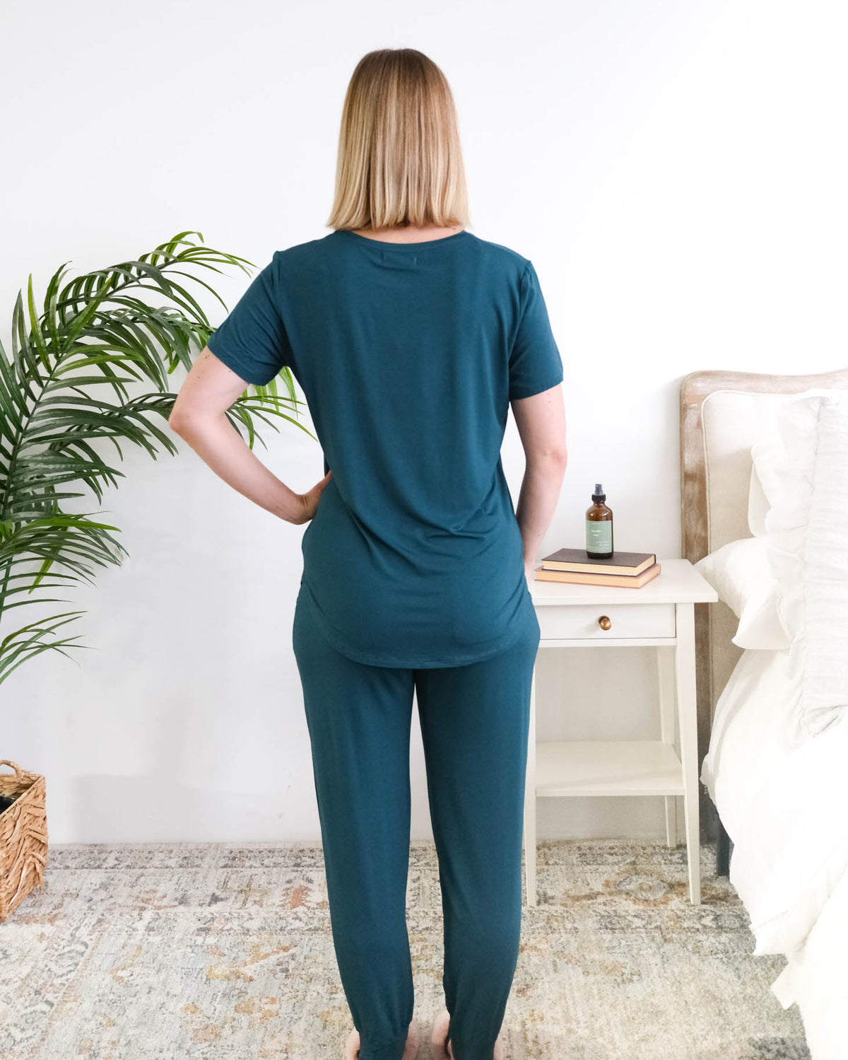 Back view of the Midnight Teal Tee/Jogger PJ Set, showing the relaxed tee length and straight jogger fit. Women is standing in a bedroom. Cloud Nine Pajamas Edmonton