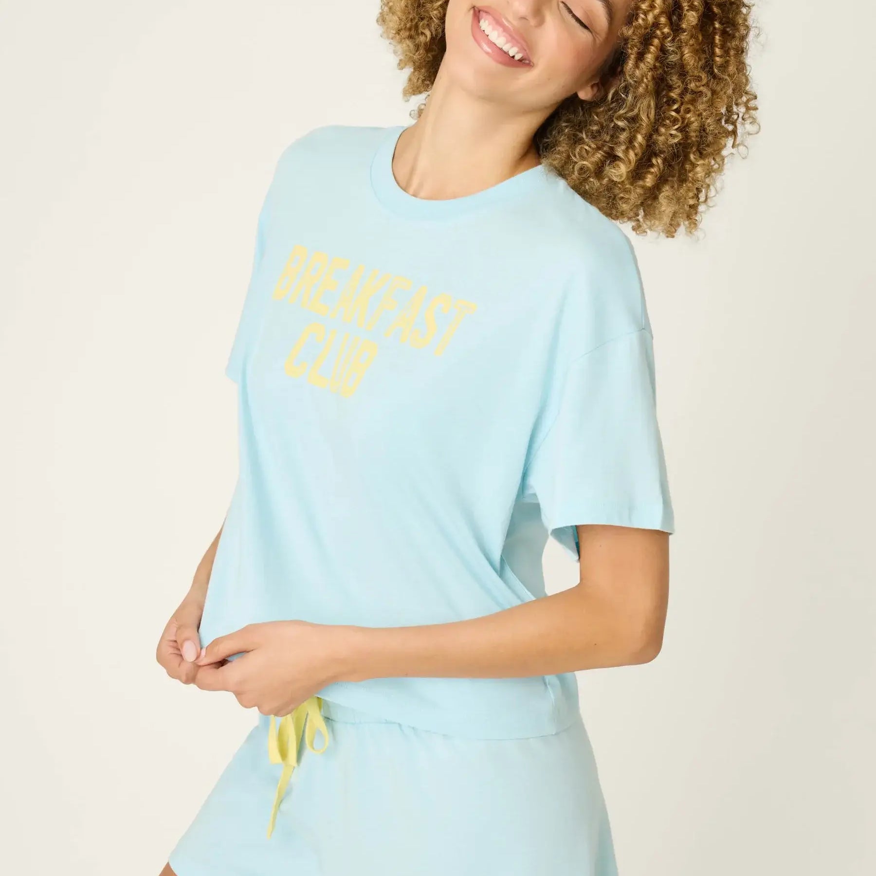 PJ SALVAGE Graphic Print Softee Tee & Short Lounge Set in "Breakfast Club" graphic tee shirt in light blue. Model stands against a light background in a lifestyle profile shot