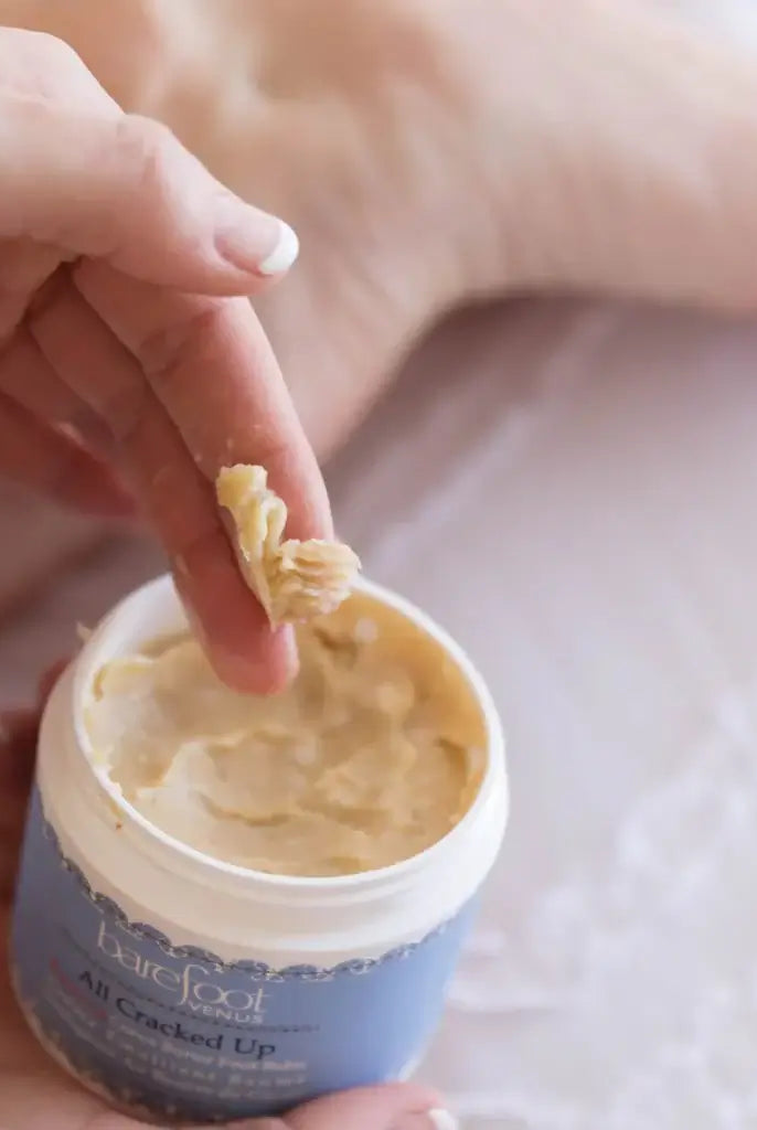 Person applying All Cracked Up Foot Balm from a jar, showcasing its rich texture and soothing properties.