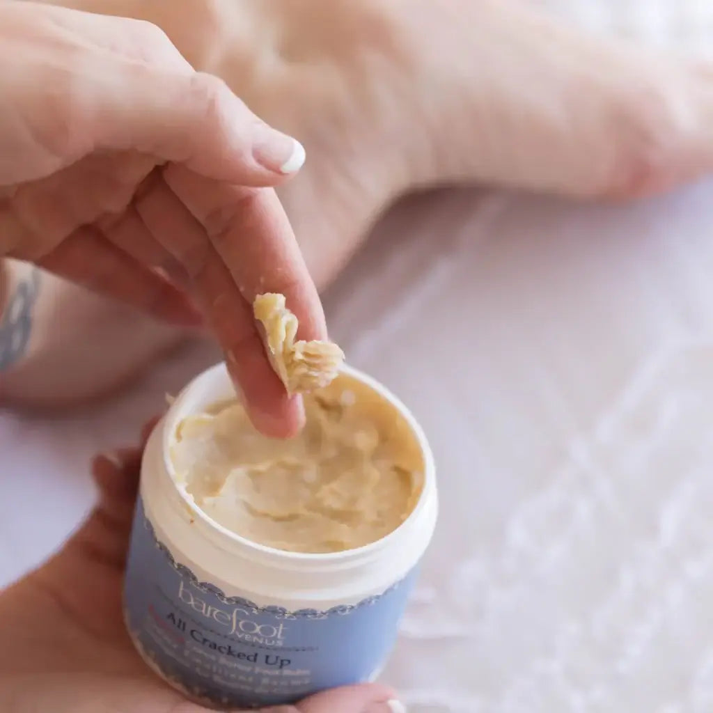 Person applying All Cracked Up Foot Balm from a jar, showcasing its rich texture and soothing properties.
