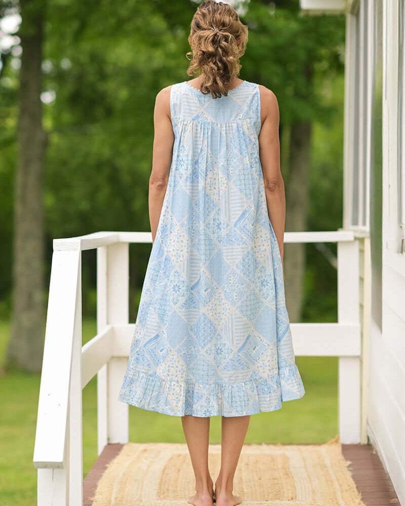 Showing the back of the April Cornell Maddie’s Medley Cotton Nightgown – Embroidered Light Blue Sleeveless Nighty with Button Front. Worn by a model in a cottage/outdoor setting