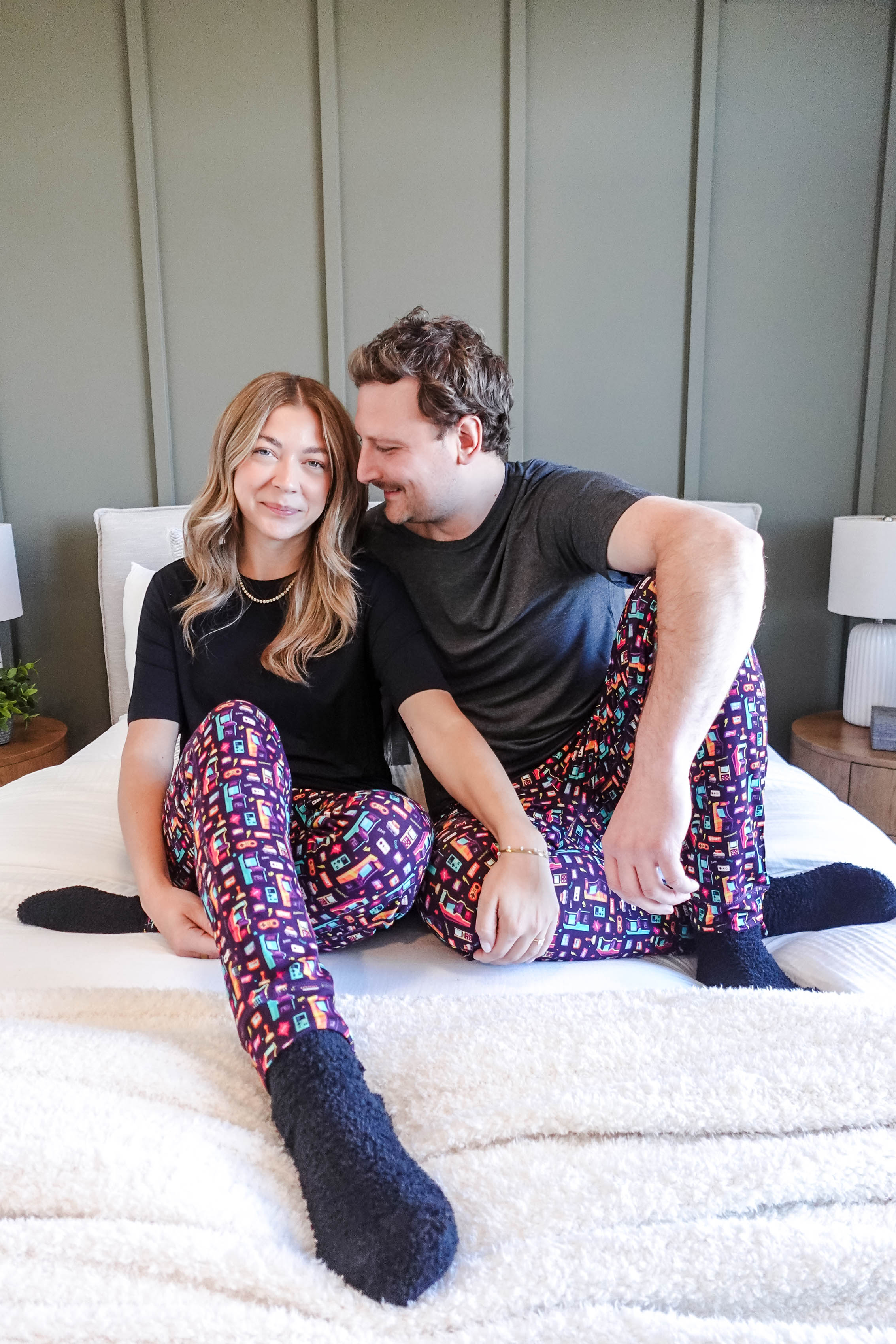 Couple wearing Arcade After Dark Unisex Bamboo Jogger lounging on a bed, showcasing colorful pajama pants.