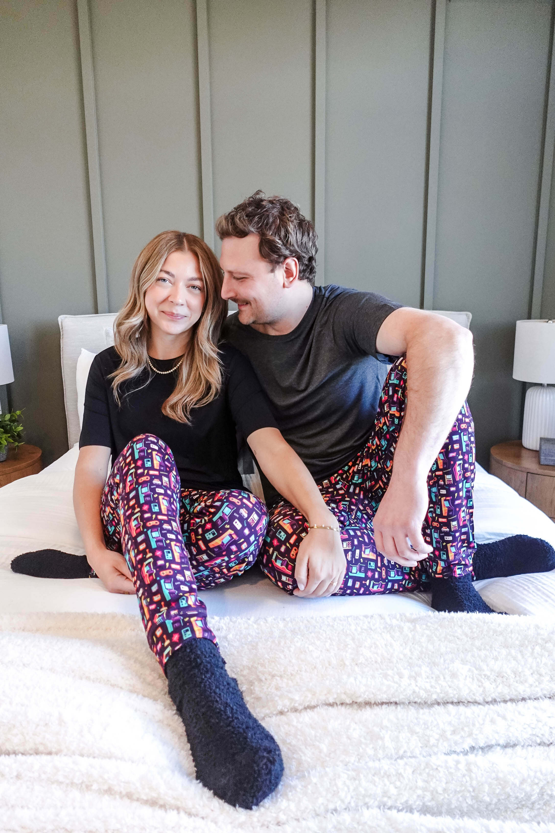 Couple wearing Arcade After Dark Unisex Bamboo Jogger lounging on a bed, showcasing colorful pajama pants.