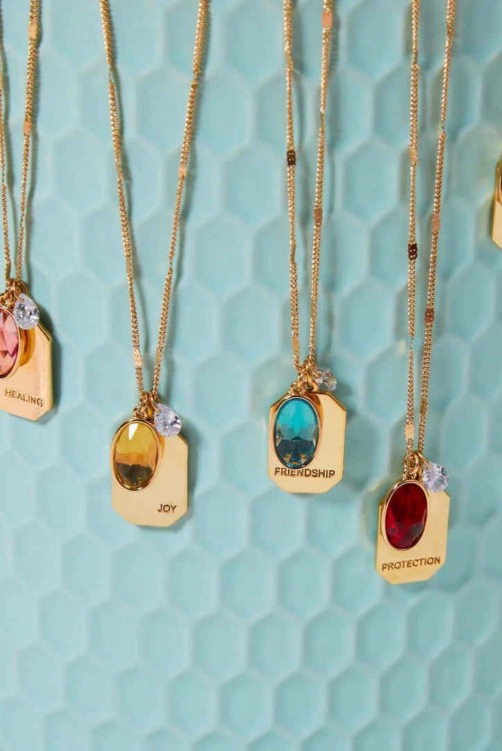 all-groups Birthstone Charm Necklace in 14k Plated Gold with oval-cut stones and intention words displayed on a blue background.