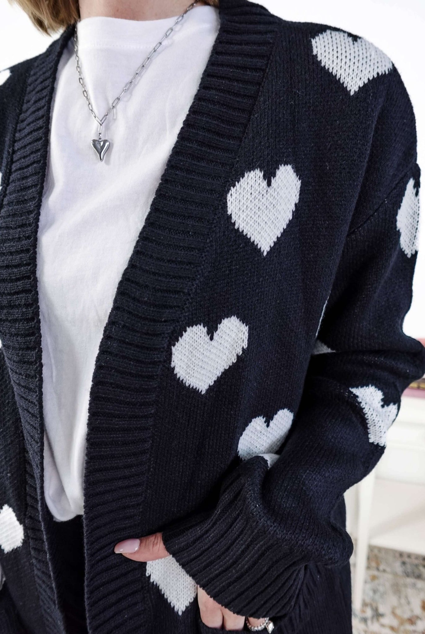 Scarlett Ellie Black Hearts Knit Cardigan | Cloud Nine Pajamas Women standing in a long black open cardigan with white hearts on it in a bedroom