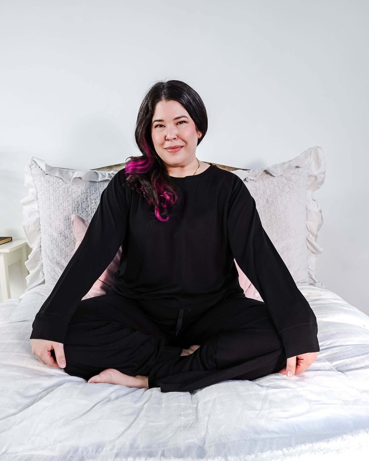 Woman sitting cross-legged on a bed in the black Cloud Soft Raw Edge Bamboo Lounge Set