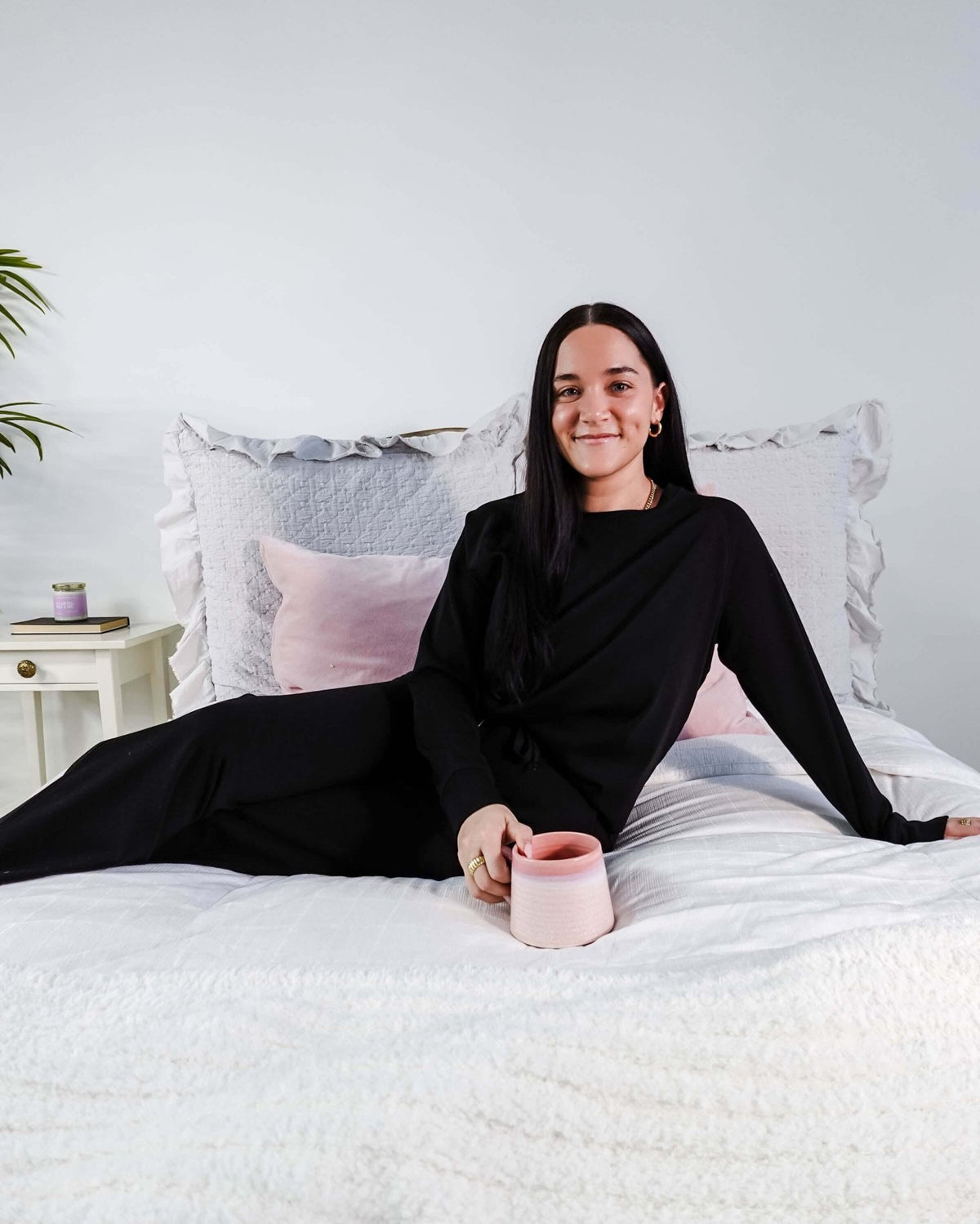 Woman lounging on a bed with a pink mug in the black Cloud Soft Raw Edge Bamboo Lounge Set