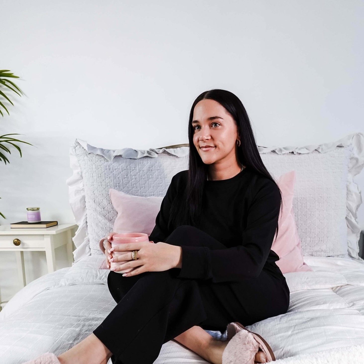 Woman wearing Black Long Sleeve Raw Edge Straight Pant Cloud Lounge Set seated on a bed holding a drink.