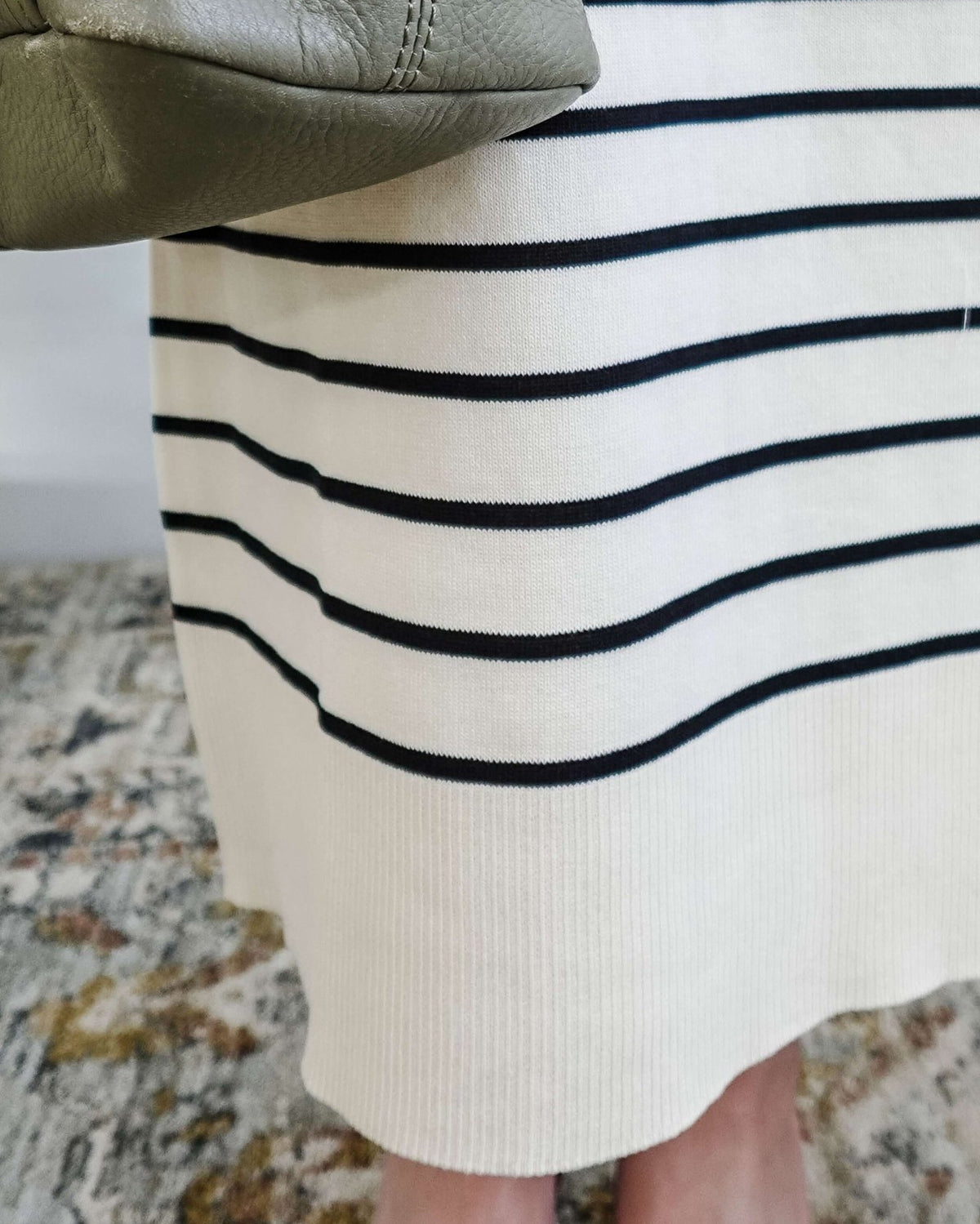 Close-up of a person wearing a white skirt with black stripes and a green purse