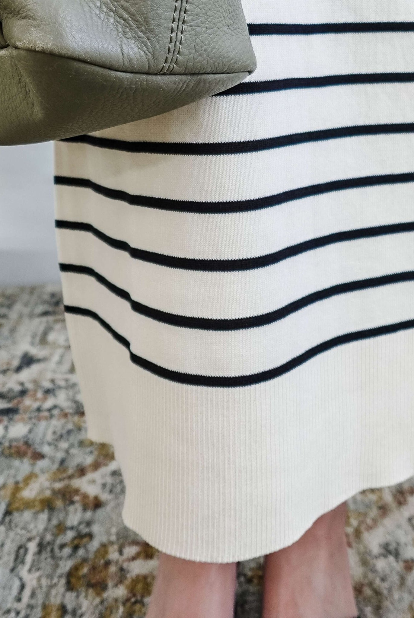 Close-up of a person wearing a white skirt with black stripes and a green purse