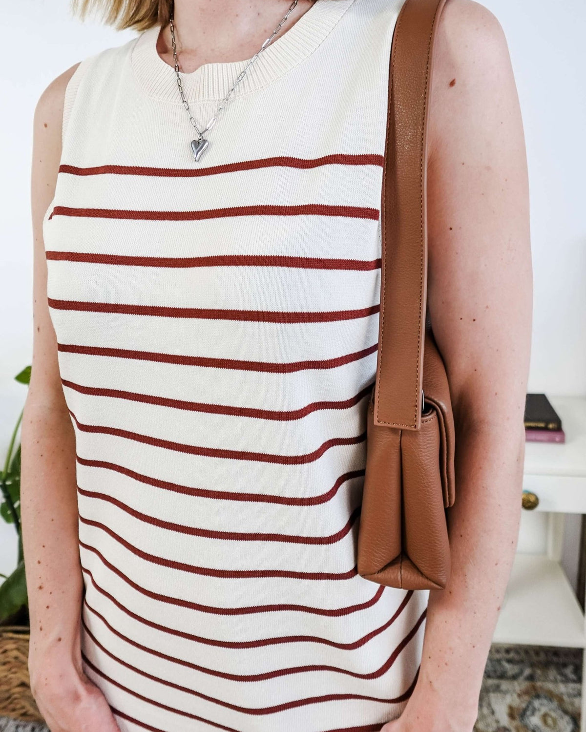 Person wearing a white sleeveless dress with brown stripes and carrying a brown bag.