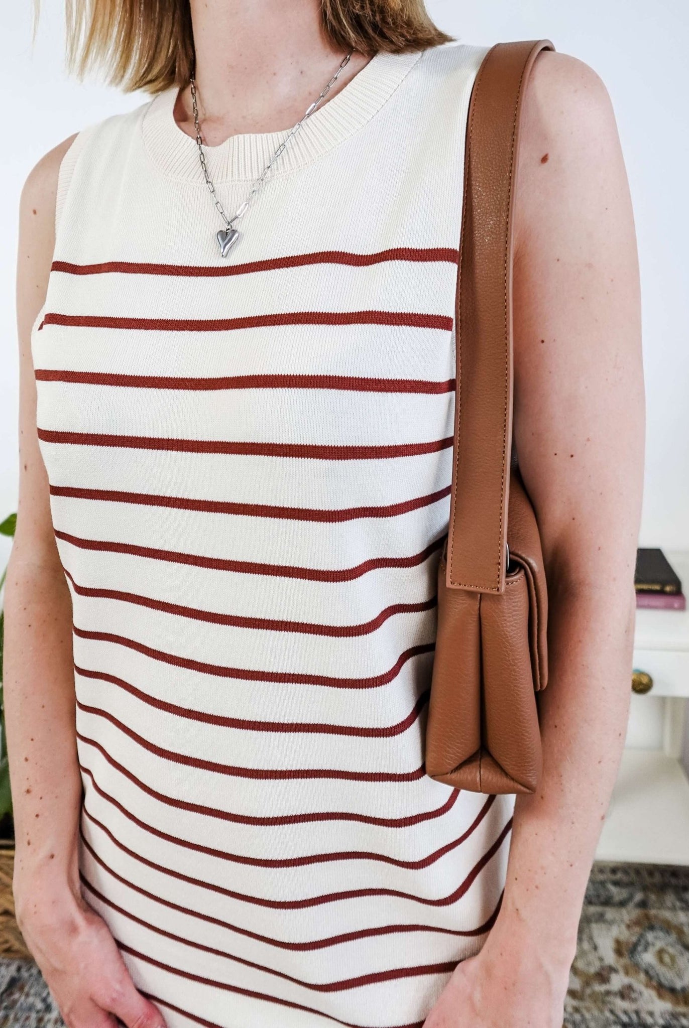 Person wearing a white sleeveless dress with brown stripes and carrying a brown bag.