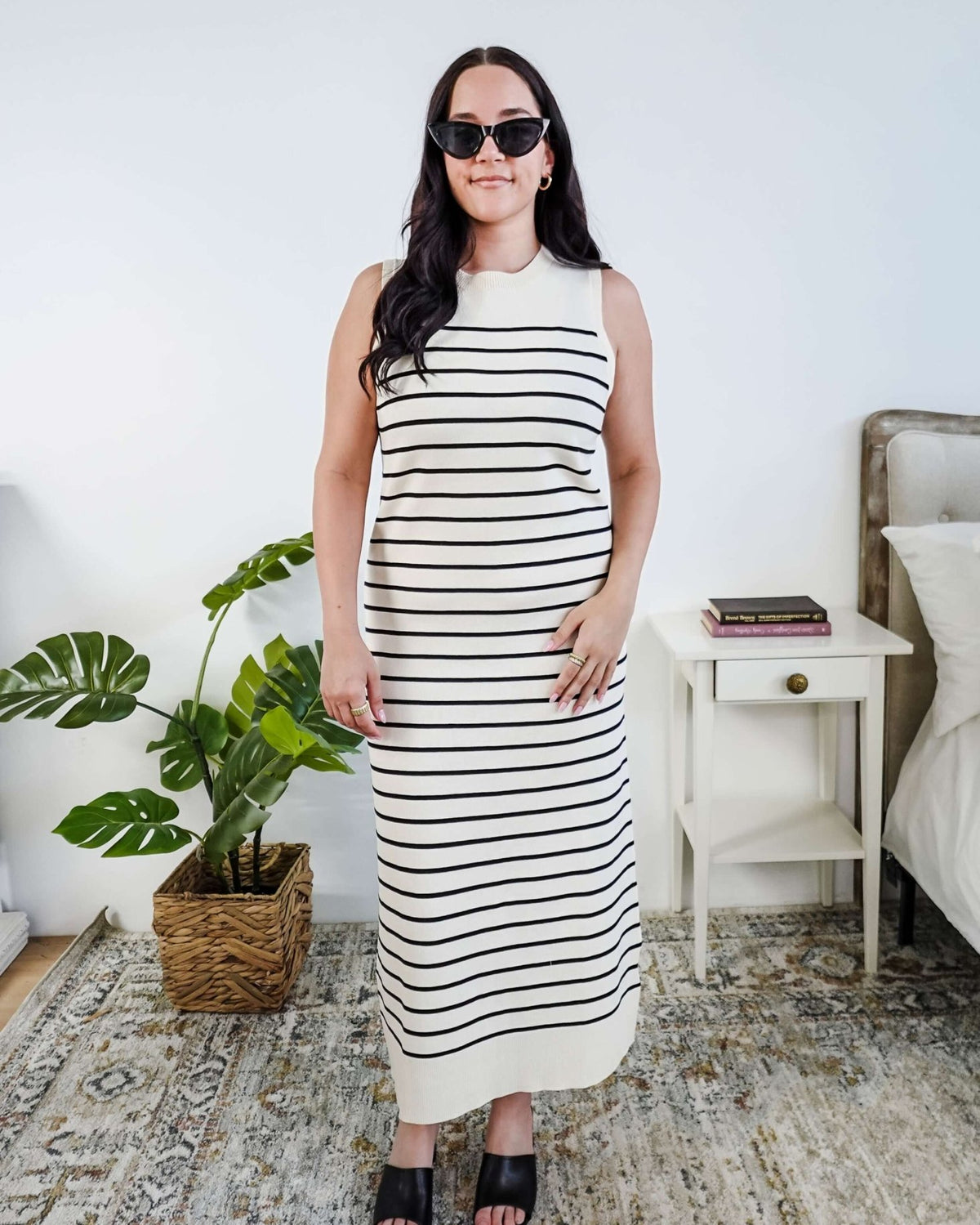 Woman wearing a black and white striped knit dress in a bedroom setting.