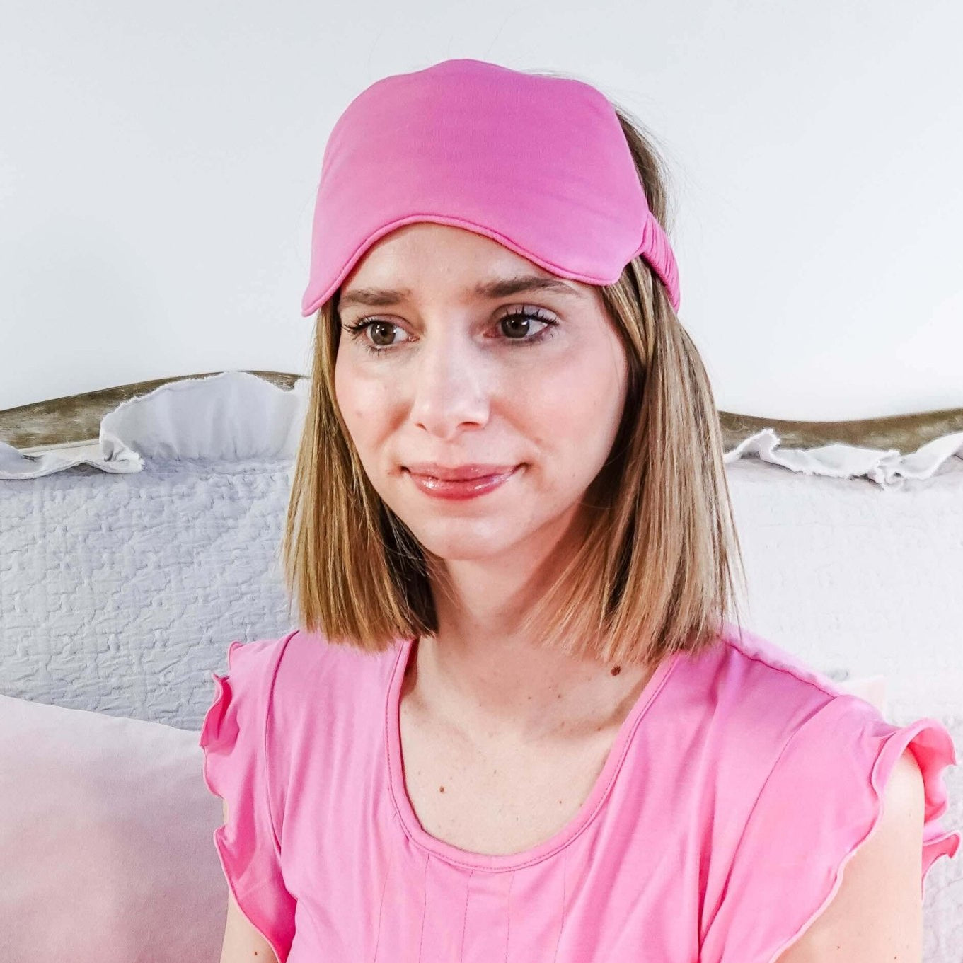 Woman wearing Bubblegum Pink Bamboo Sleep Eye Mask while holding a pink mug, sitting on a bed.