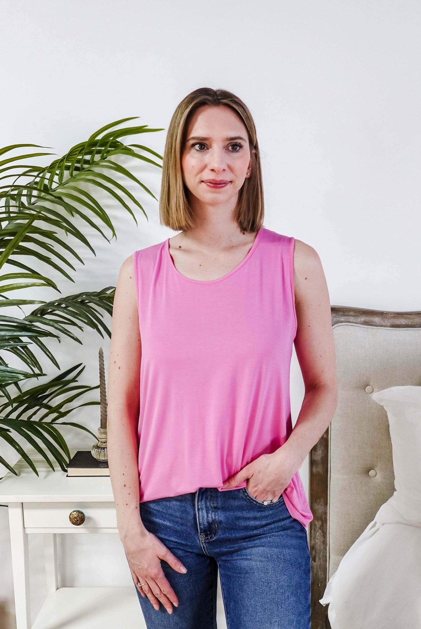 Model wearing the Bubblegum Pink Essential Bamboo Tank Top with jeans and a plant in the background.