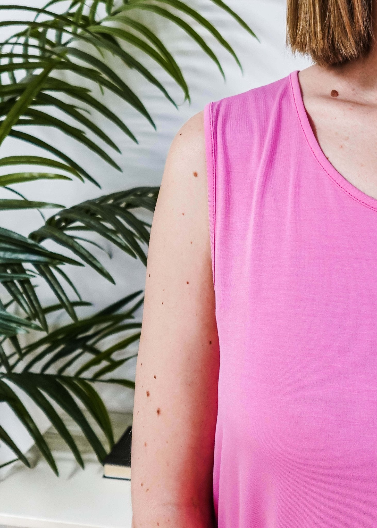 Close-up of a woman wearing the Bubblegum Pink Essential Bamboo Tank Top next to a green plant.
