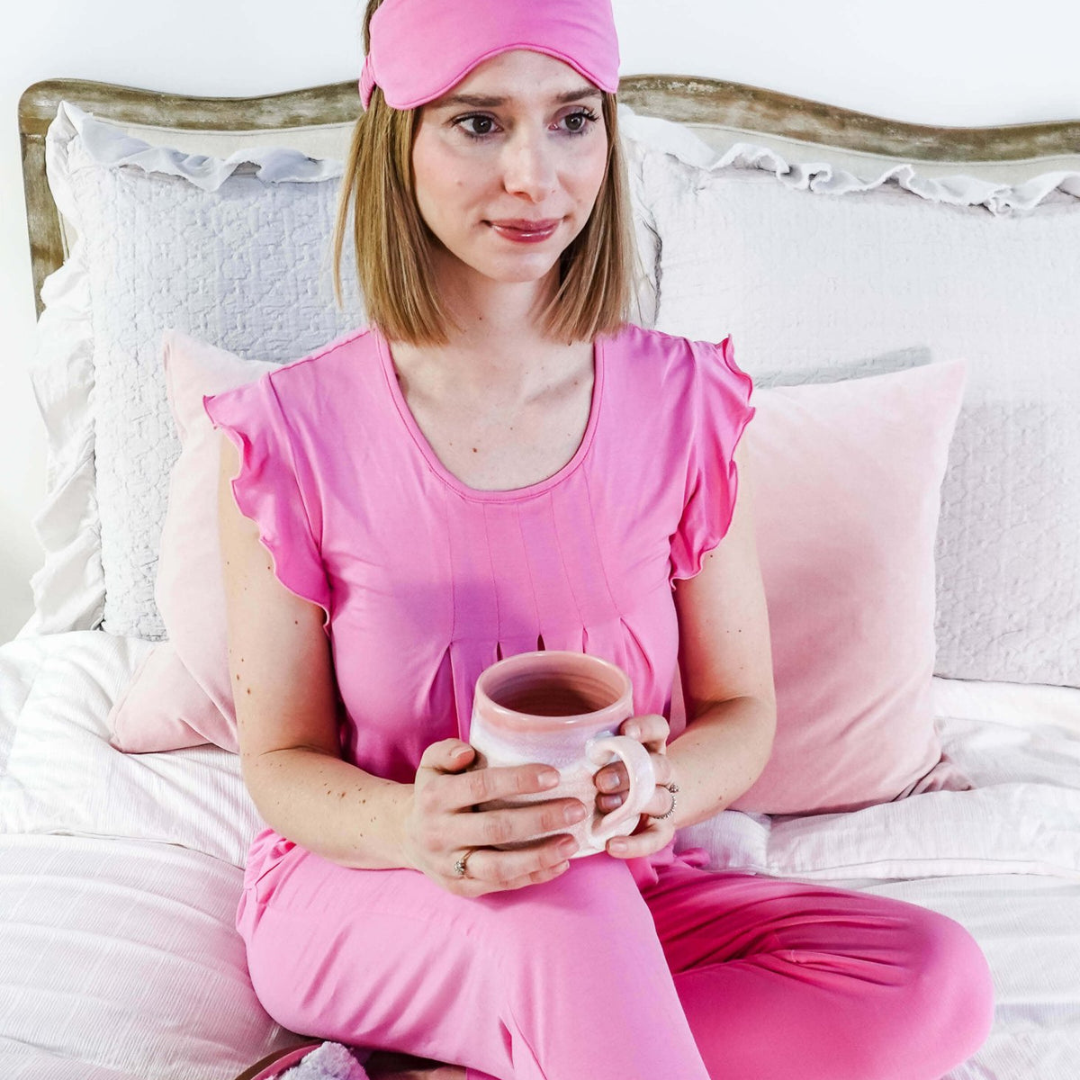 Woman in Bubblegum Pink Flutter Top and Jogger Bamboo PJ Lounge Set holding a mug, relaxing on a bed.