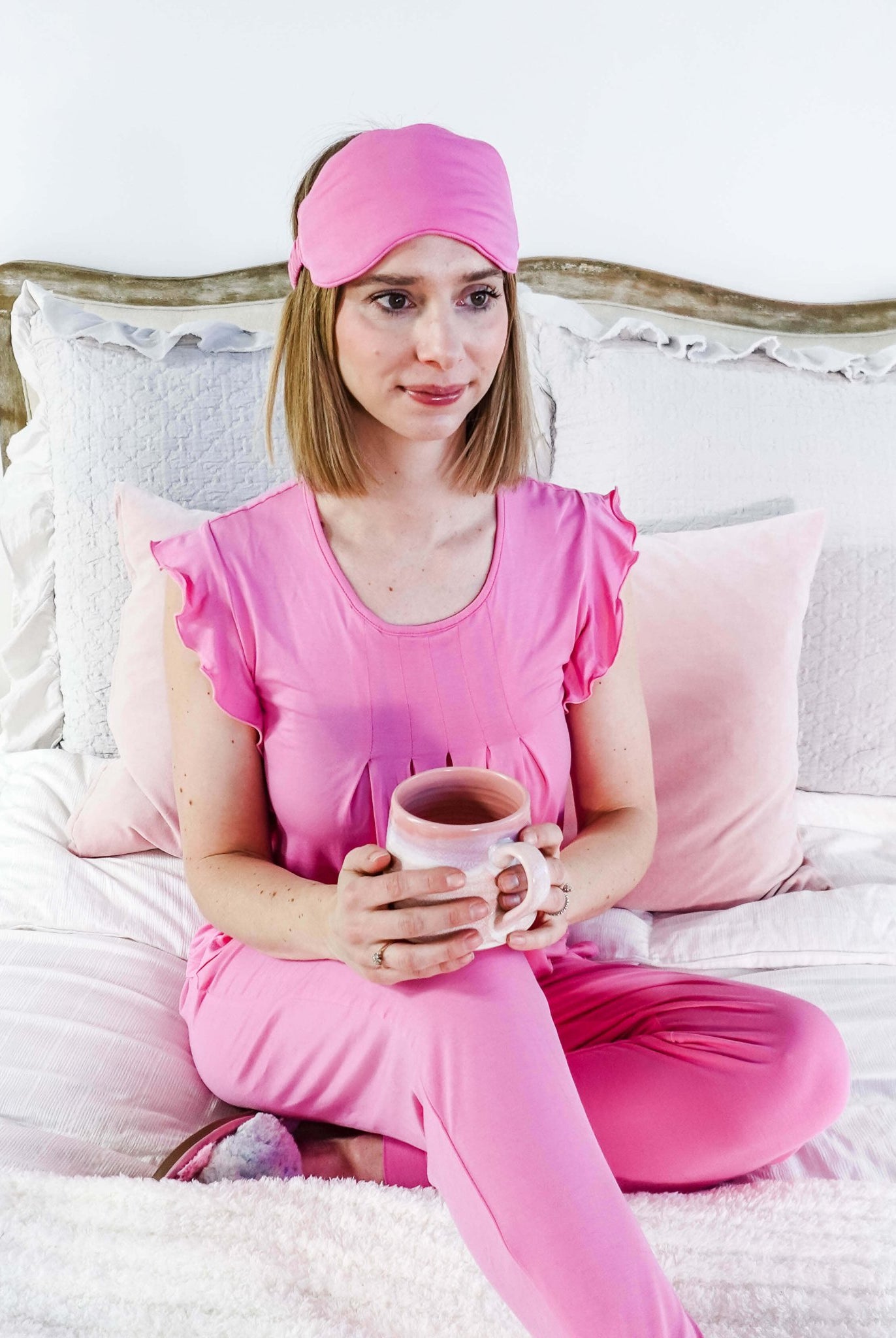 Woman in Bubblegum Pink Flutter Top and Jogger Bamboo PJ Lounge Set holding a mug, relaxing on a bed.