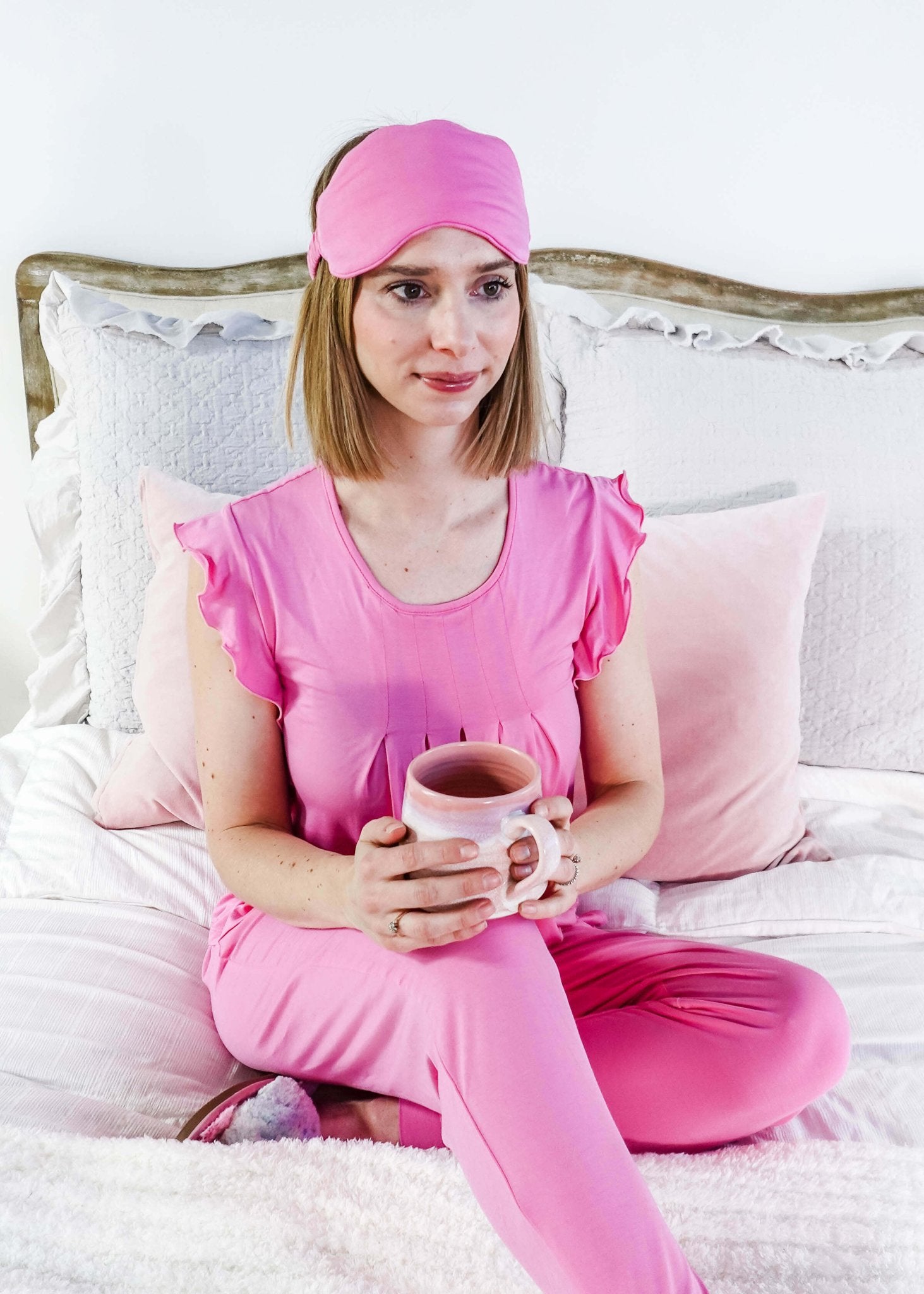 Woman in Bubblegum Pink Flutter Top and Jogger Bamboo PJ Lounge Set holding a mug, relaxing on a bed.